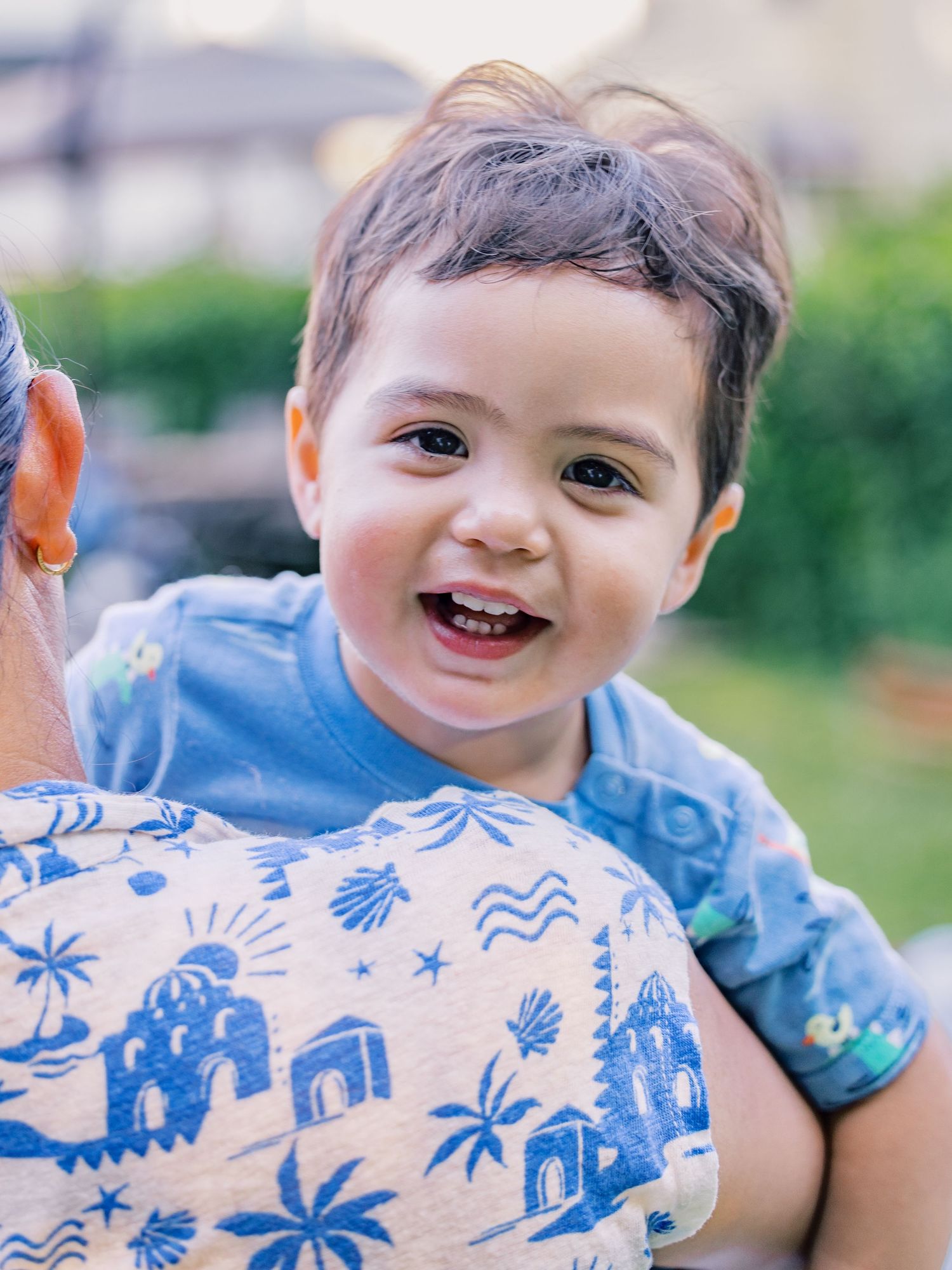 Smiling child wearing blue t-shirt with elephant and palm tree pattern in outdoor setting on sunny day.