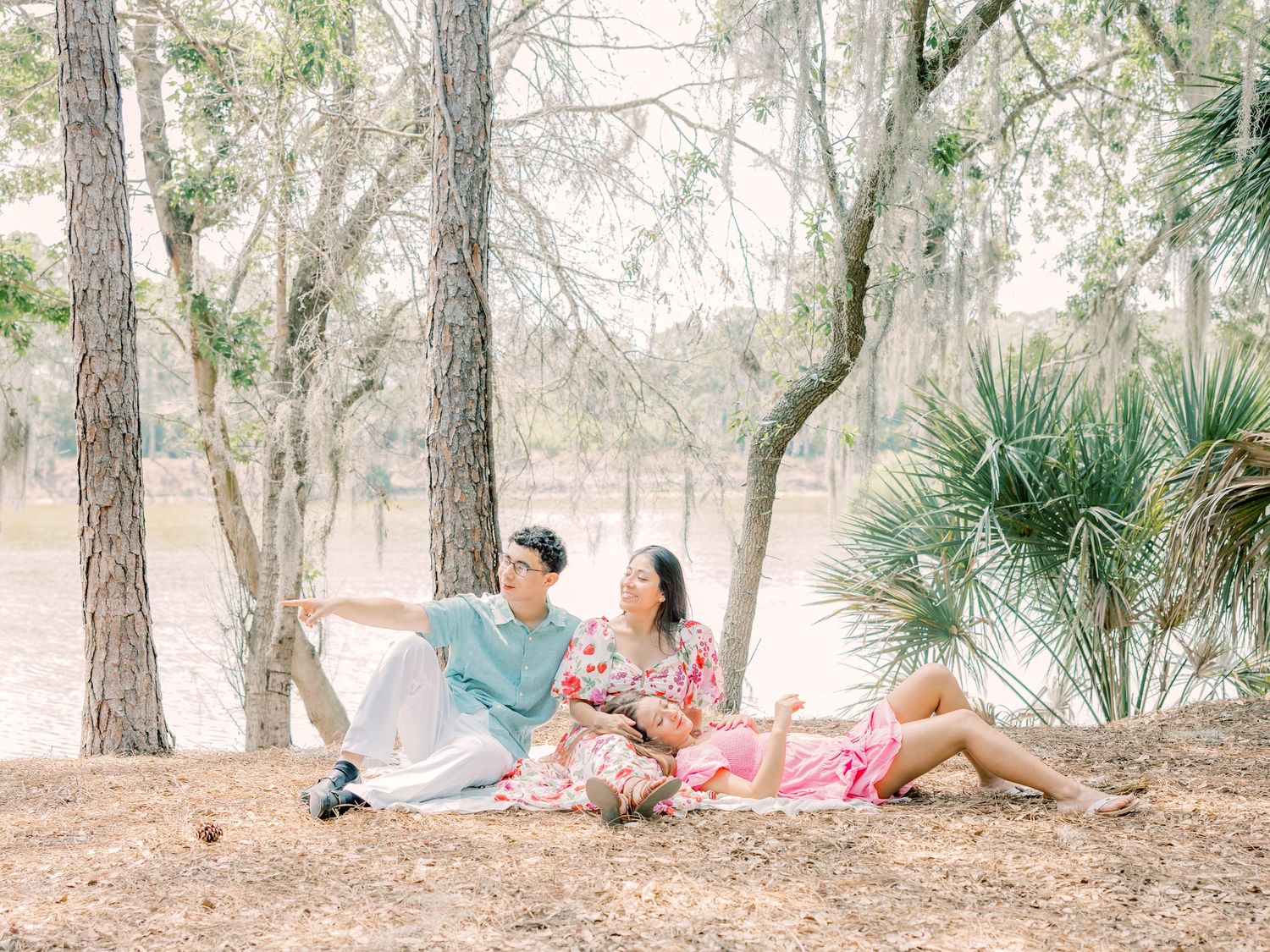 A couple lounges on a blanket for a romantic picnic among palm trees and pine trees in a serene outdoor setting.