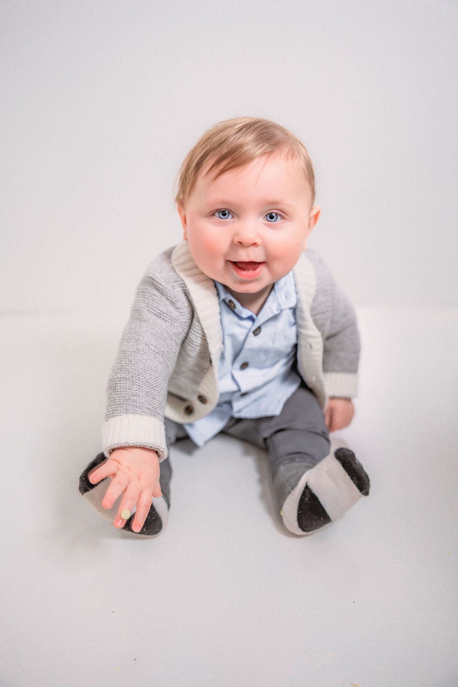 Baby in a grey sweater and blue bowtie crawling and smiling on white background showing progression of movement.