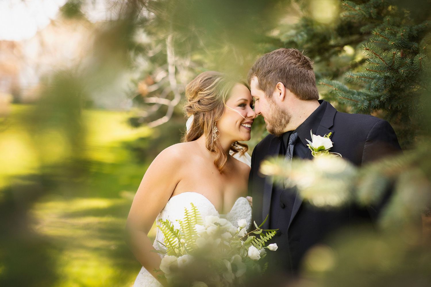 Romantic wedding photograph through leaves showing intimate moment in garden setting.