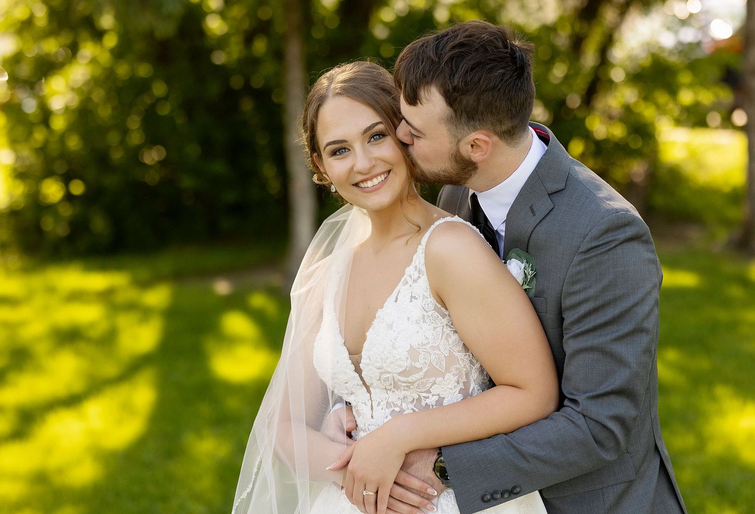 Tender wedding moment captured in sunlit garden with lace dress detail.