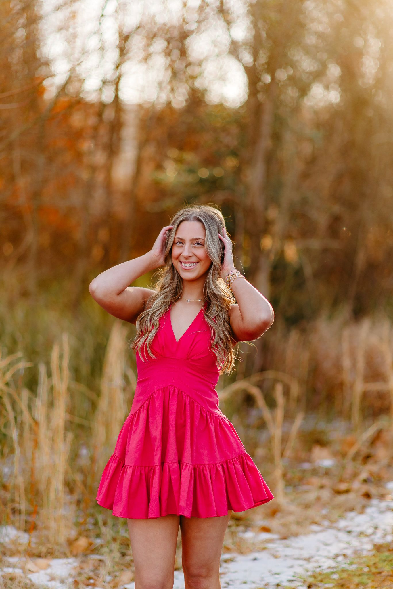 Woman in vibrant red dress laughing joyfully during autumn outdoor photoshoot.