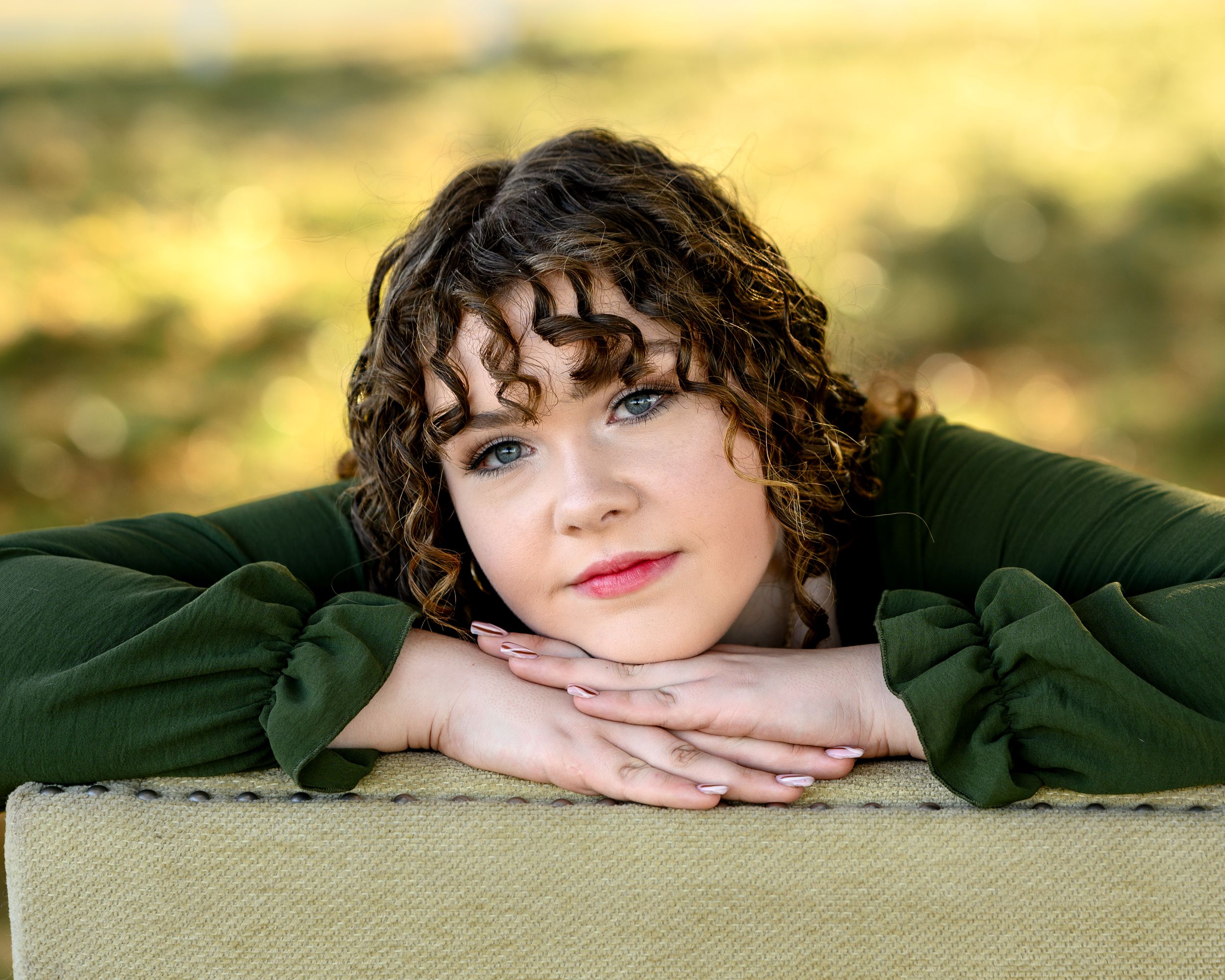 Portrait against soft golden backdrop wearing dark green sweater.
