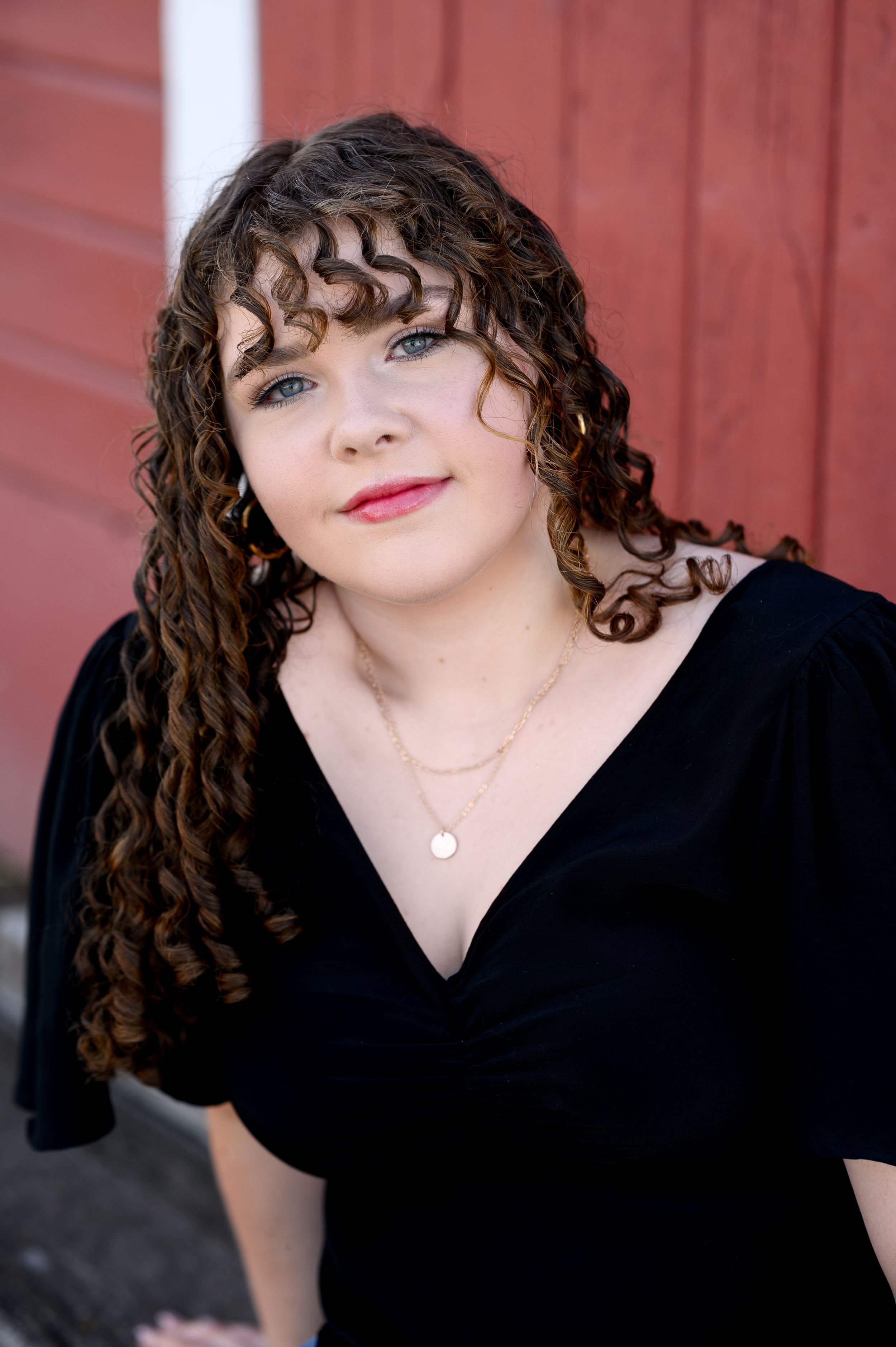Portrait against red barn wall wearing black v-neck dress.