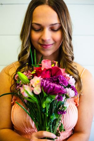 Senior girl in a peach-colored top holds a vibrant bouquet with pink, purple and white flowers, smiling with eyes closed in senior photo.