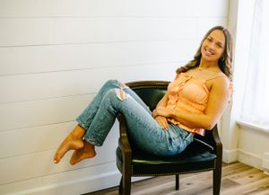 Casual senior portrait of a girl lounging in a black chair wearing a coral top and distressed jeans with Nichole Sieck Photography.