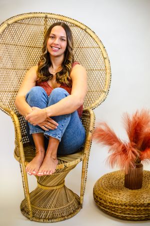 Casual portrait on wicker peacock chair with decorative accents in boho style setting in Central City photography studio with Nichole Sieck.