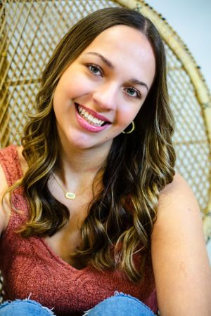 Portrait of senior girl smiling warmly while sitting in front of a woven peacock chair, wearing a rust-colored top with Nichole Sieck Photo