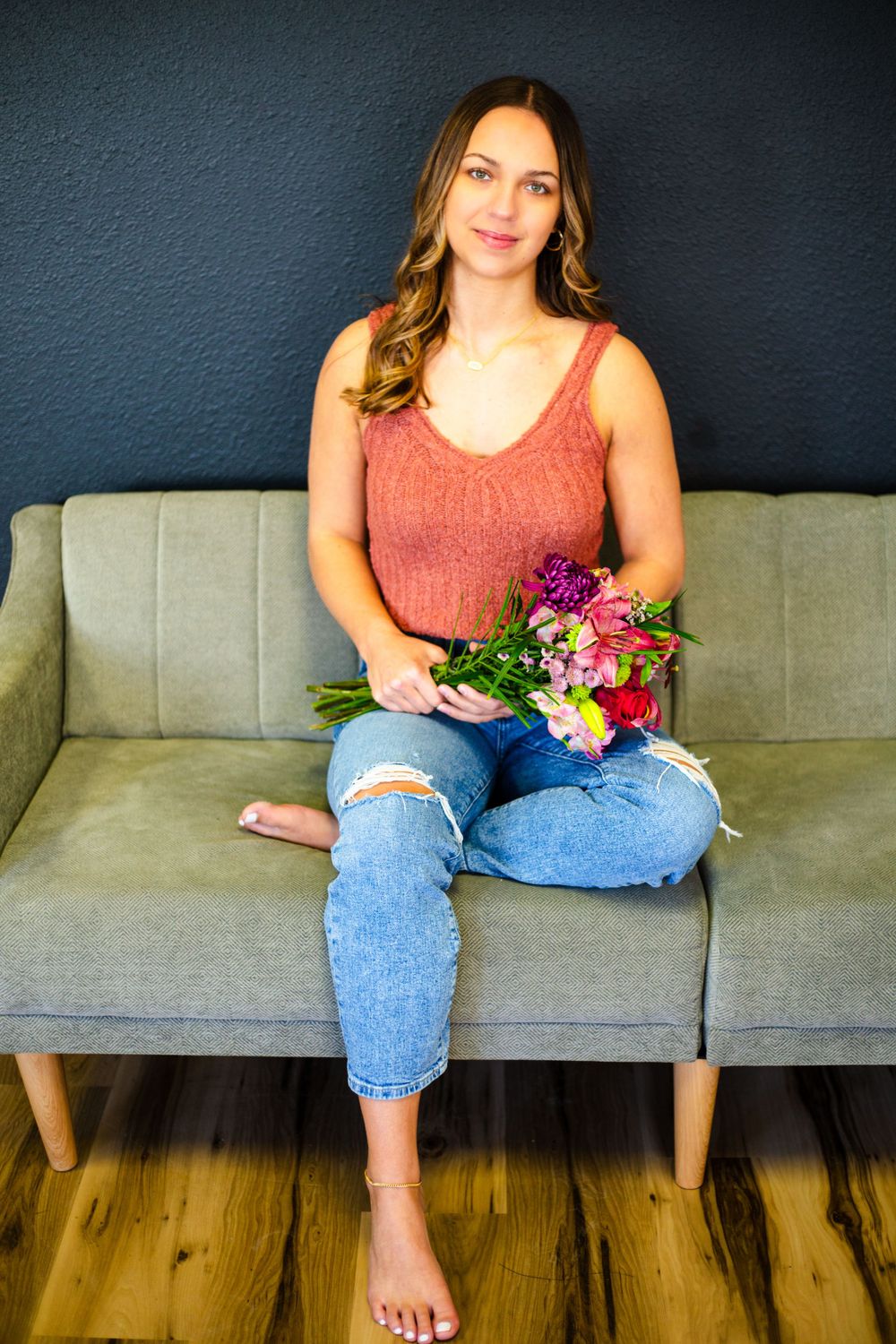 Relaxed pose on grey couch with colorful floral bouquet and distressed denim in Nichole Sieck Photography's Central City studio.