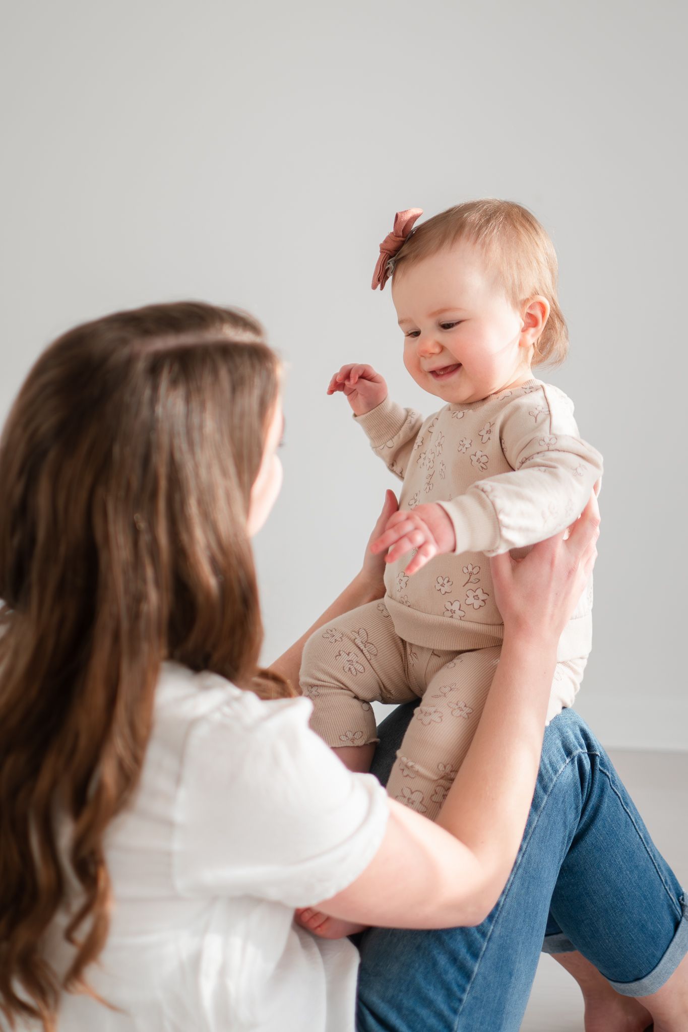 A joyful baby in beige clothing is lifted and held in the air while sharing a happy moment.