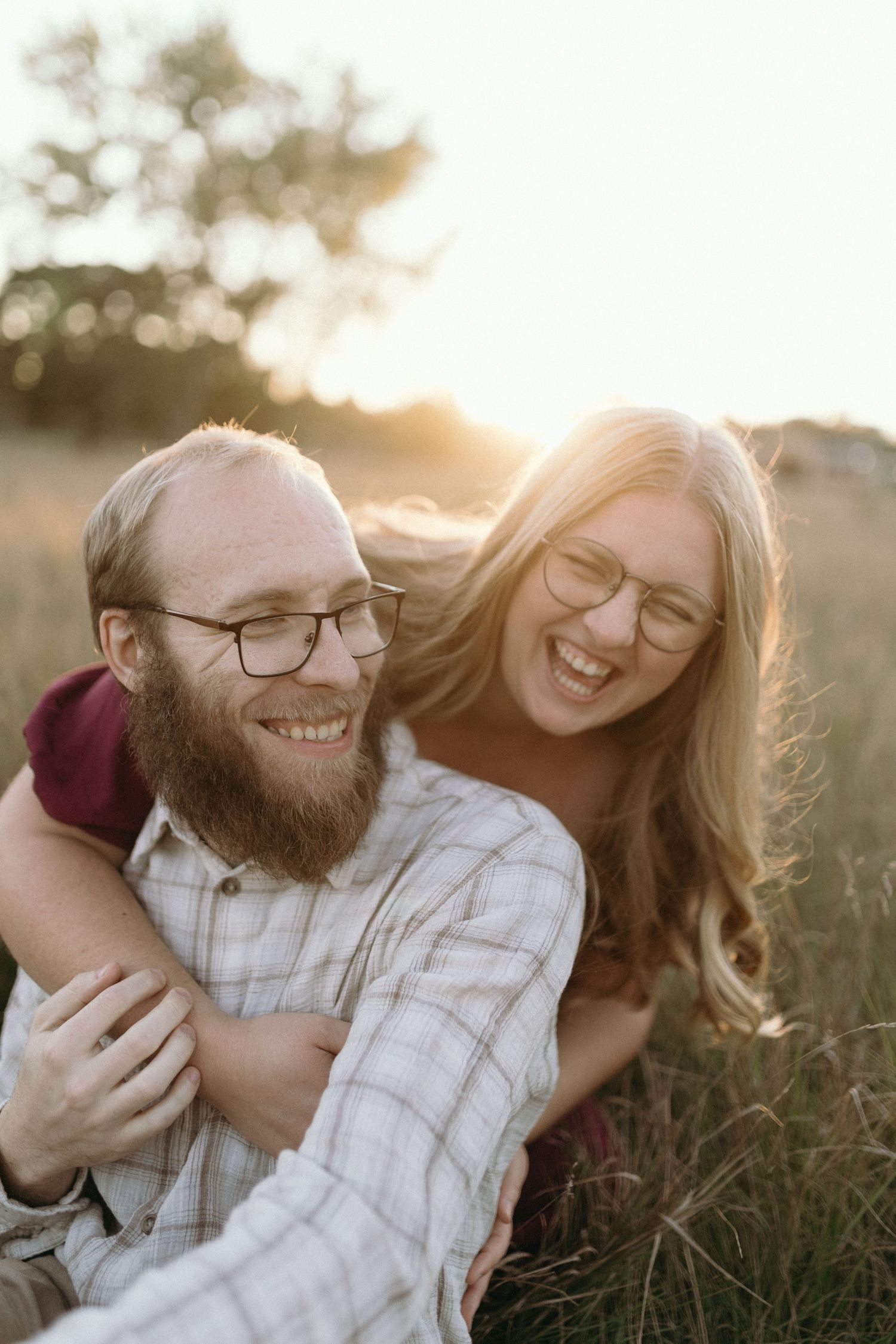 A joyful couple sharing laughter together outdoors during golden hour with sunlight creating a warm backlit glow.