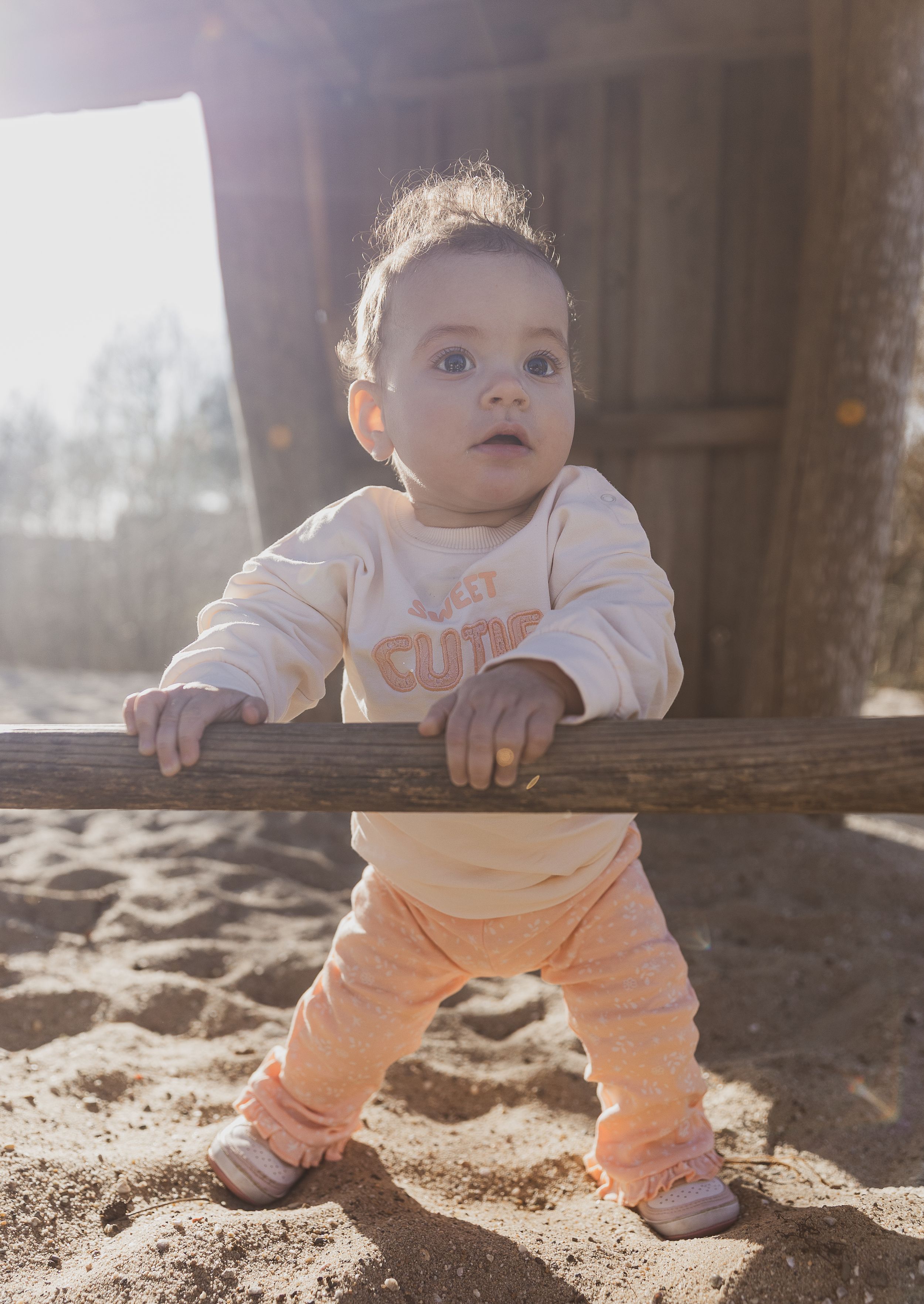 Small child in light colored outfit holding onto wooden railing while standing. campagne foto.