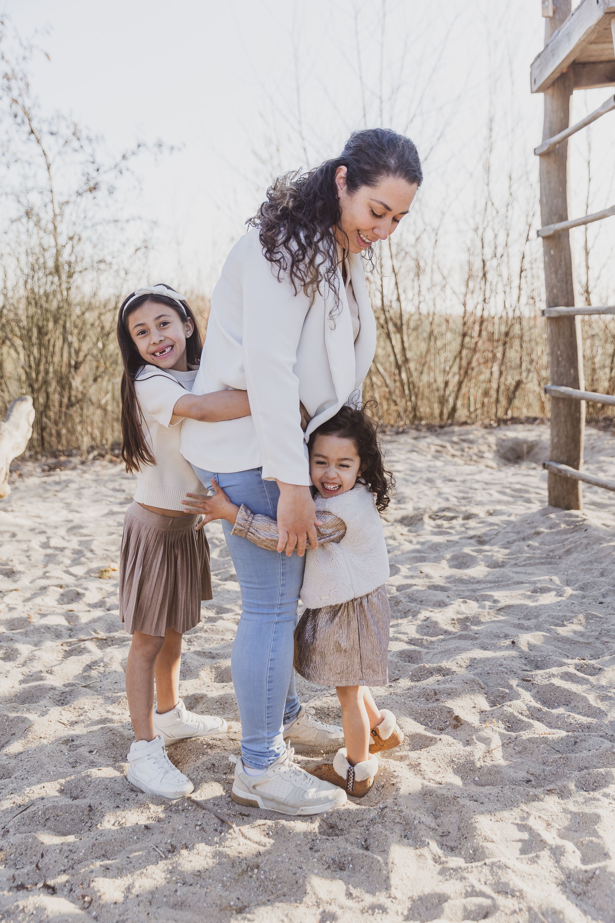 Family group enjoying a playful moment together on sandy ground near wooden structure. bijzonder moment fotografie
