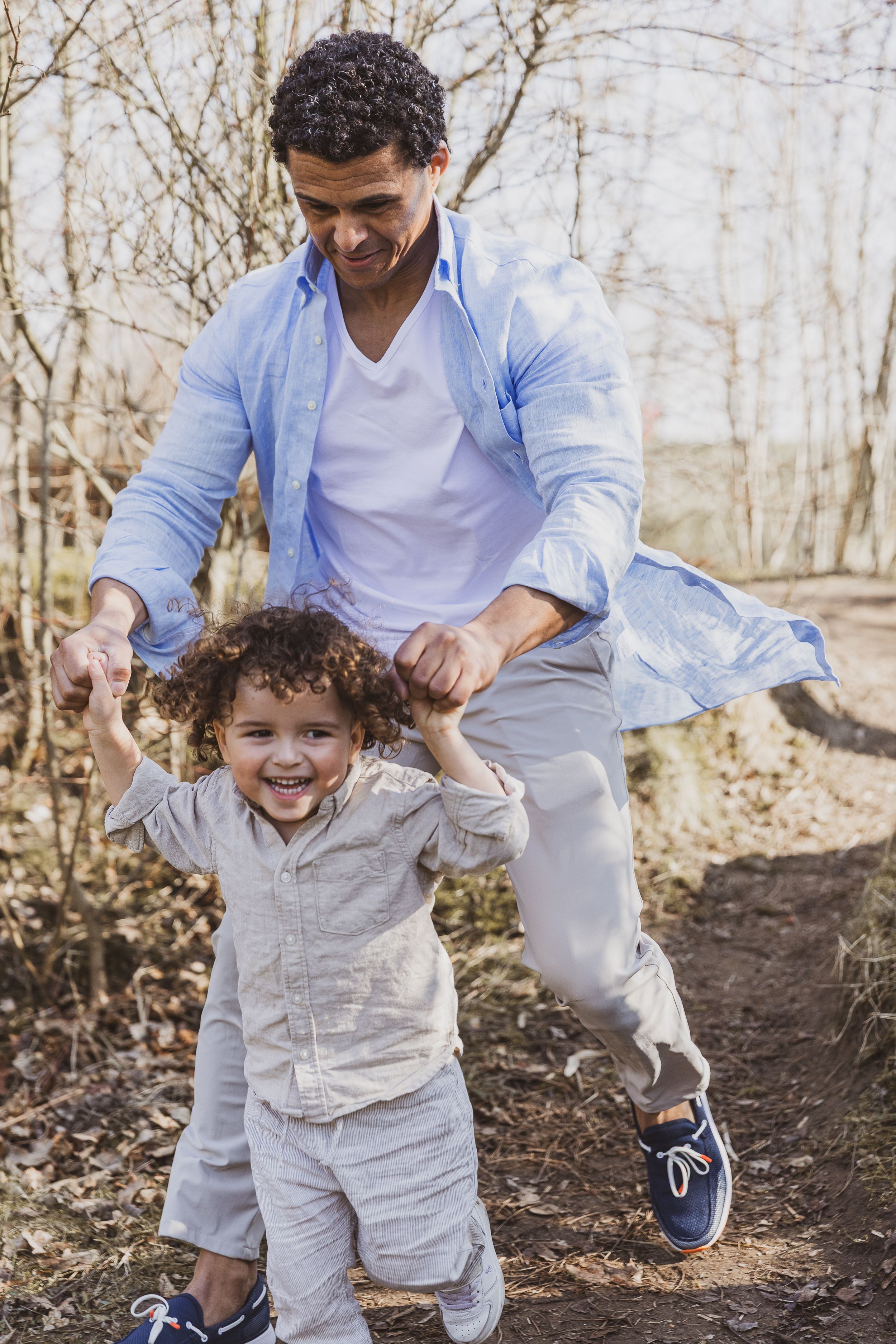 Playful moment between parent and child running through wooded area. Vader en zoon fotografie.