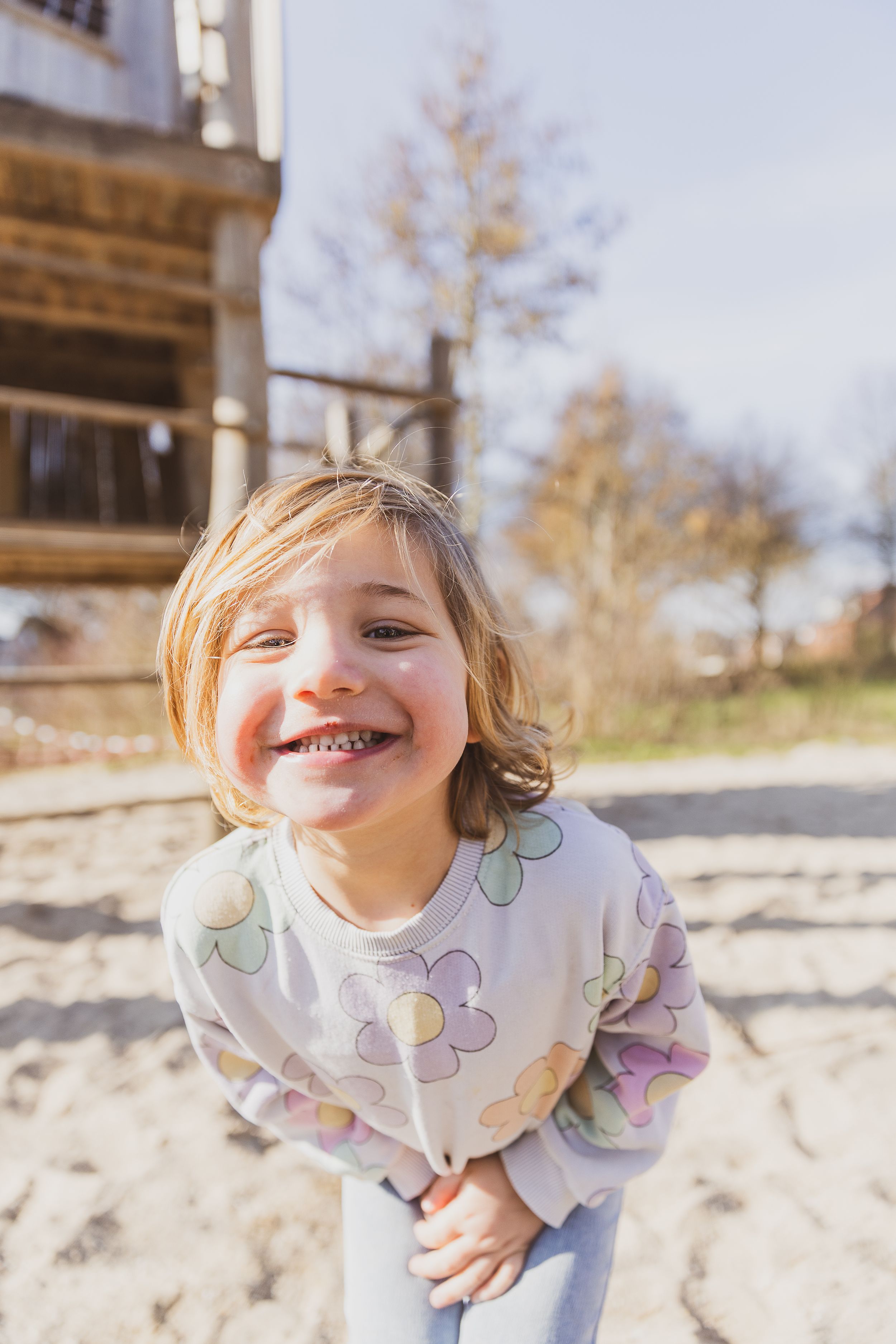 Child wearing floral sweater smiles brightly outdoors on sunny day. kinderportret