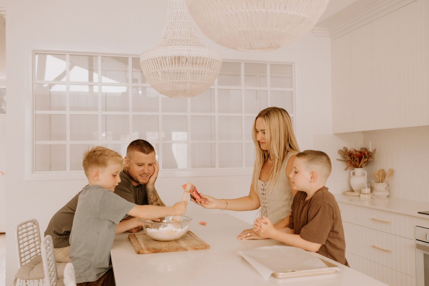Group gathers around white kitchen table for morning activities in bright modern home interior.