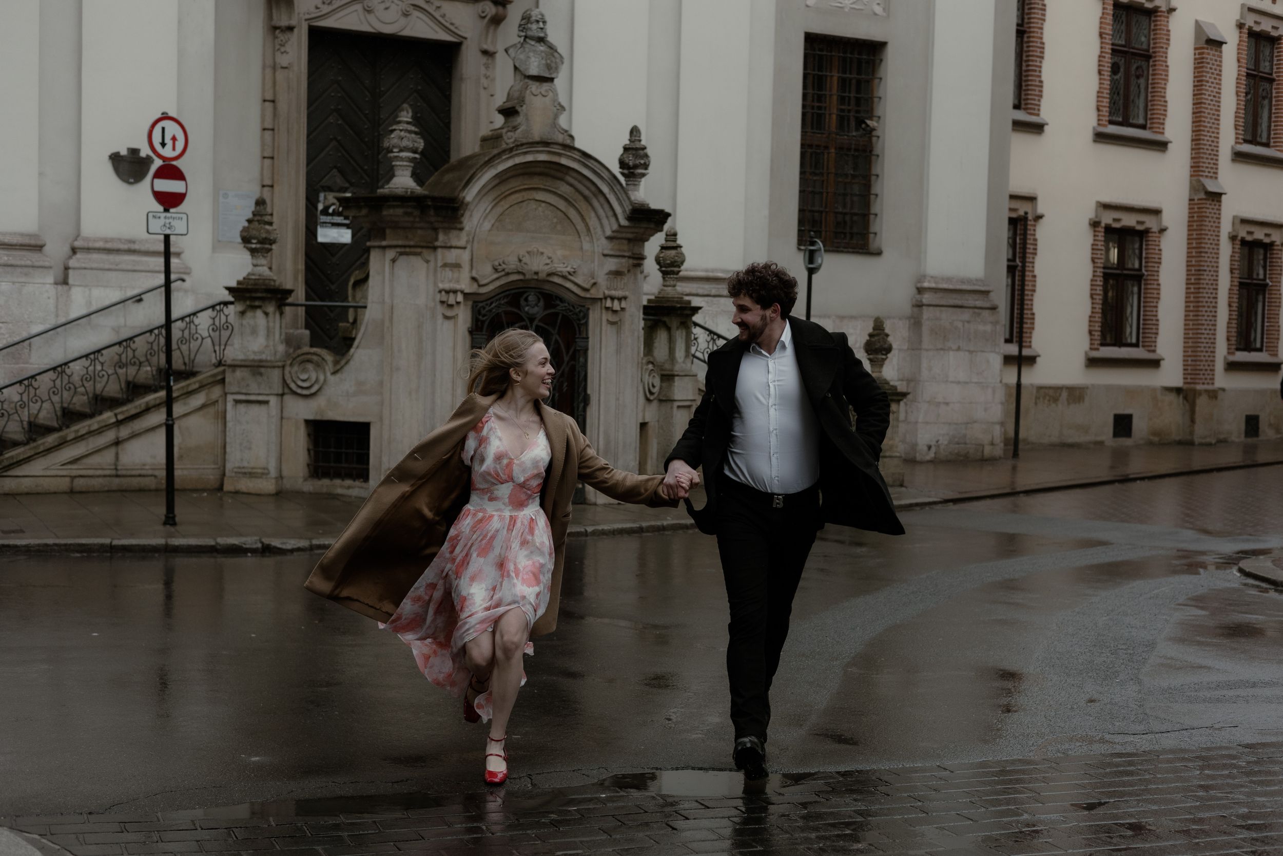 A couple runs playfully through rainy streets of an old European city in romantic vintage style.