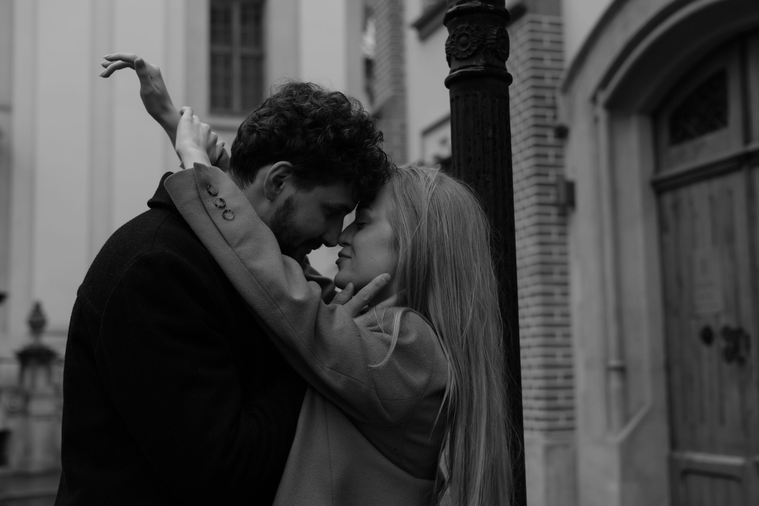 A romantic black and white moment captured between a couple embracing and kissing on an urban street.