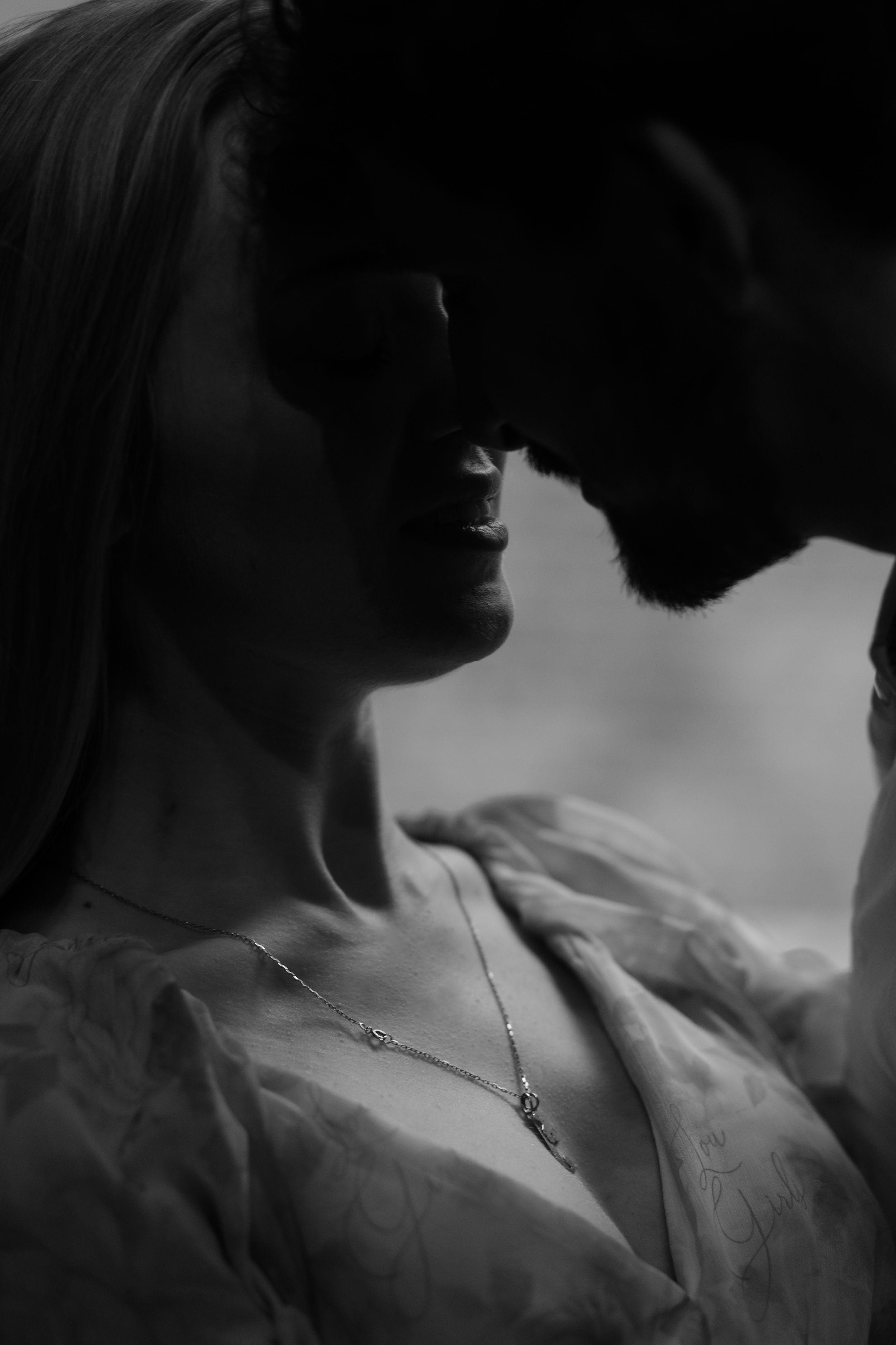 A romantic black and white portrait of a couple in an intimate moment, with soft lighting creating dramatic shadows.