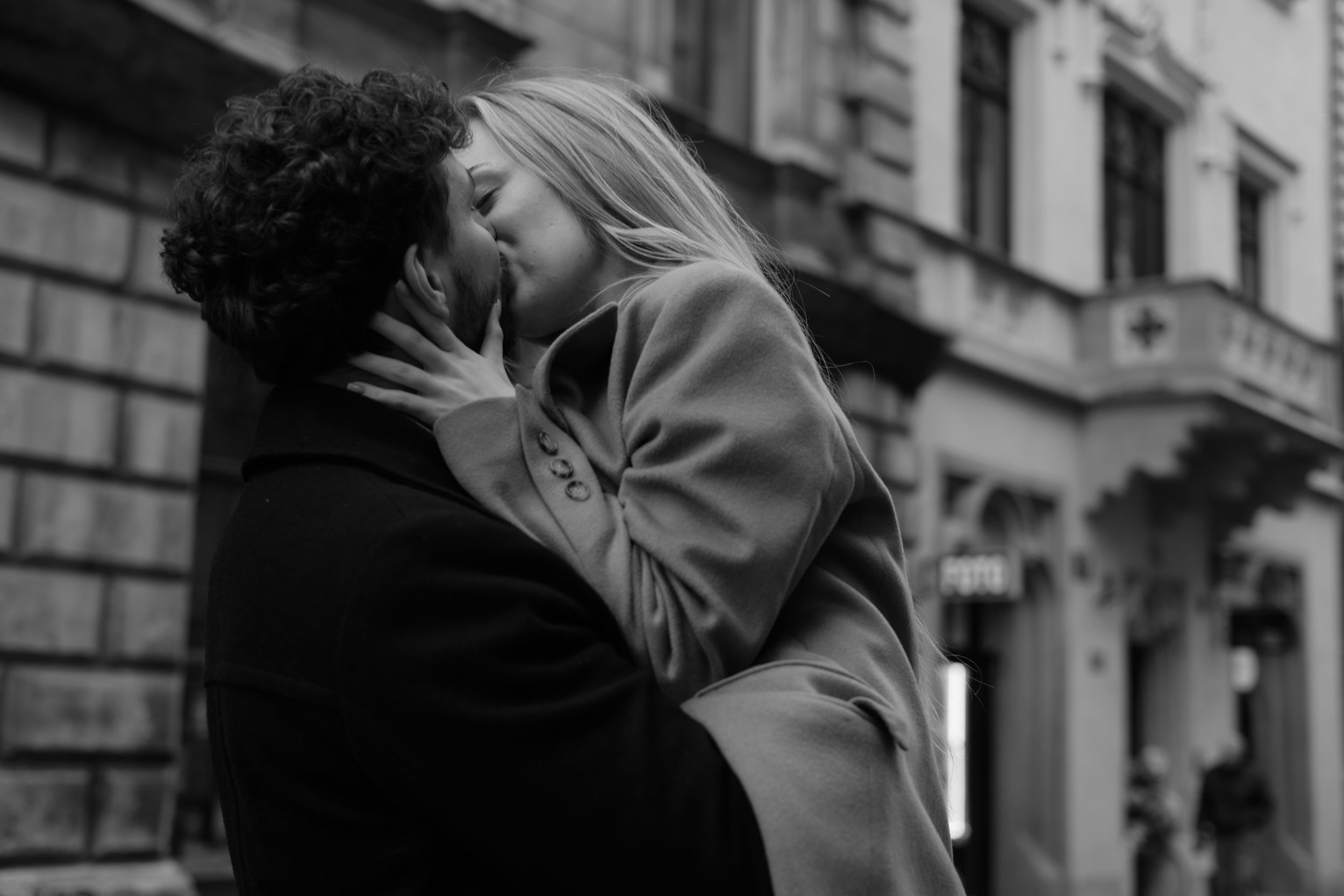 A romantic black and white photograph shows a passionate embrace between a couple on a city street.