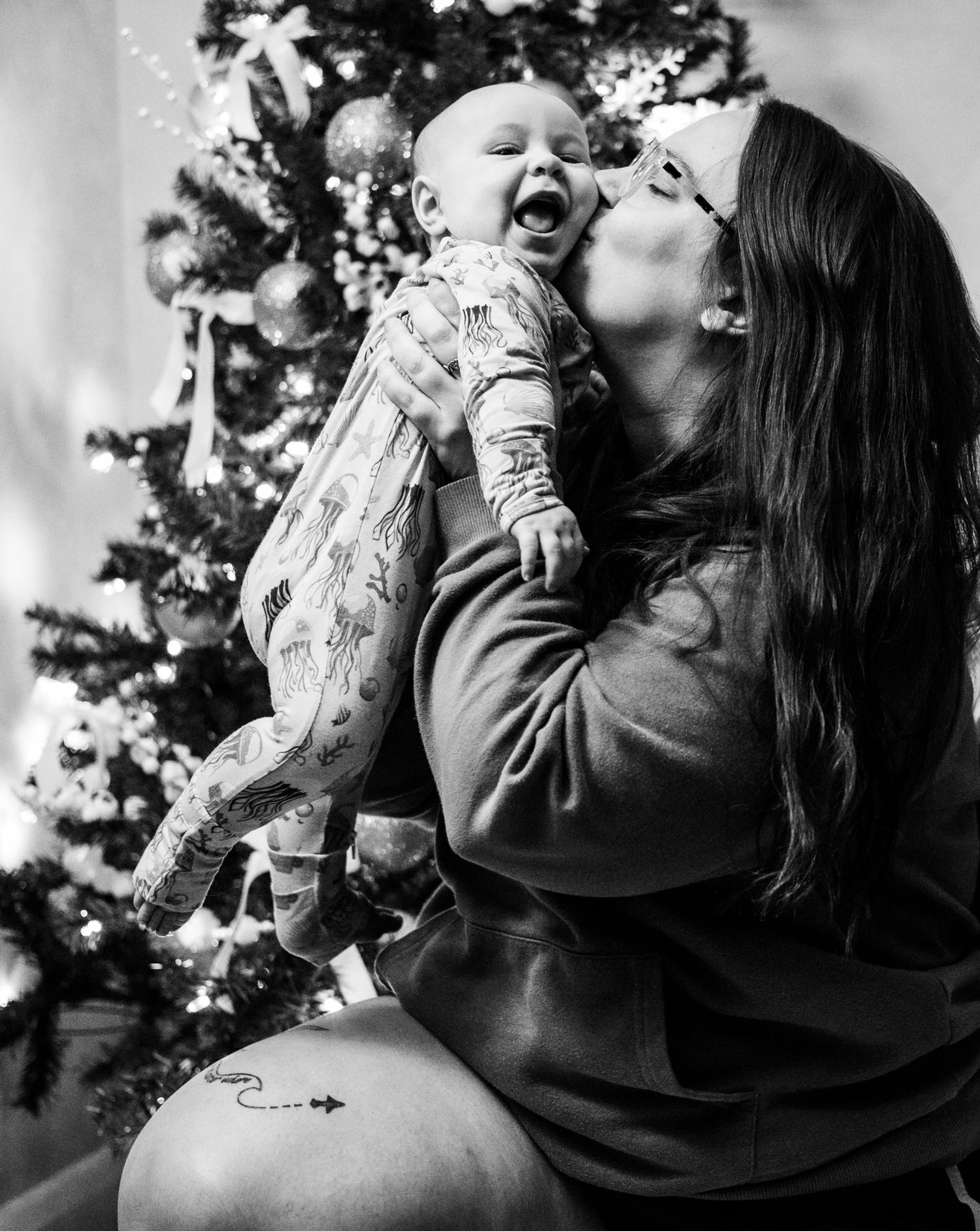 Heartwarming holiday moment between parent and baby in front of a decorated Christmas tree.