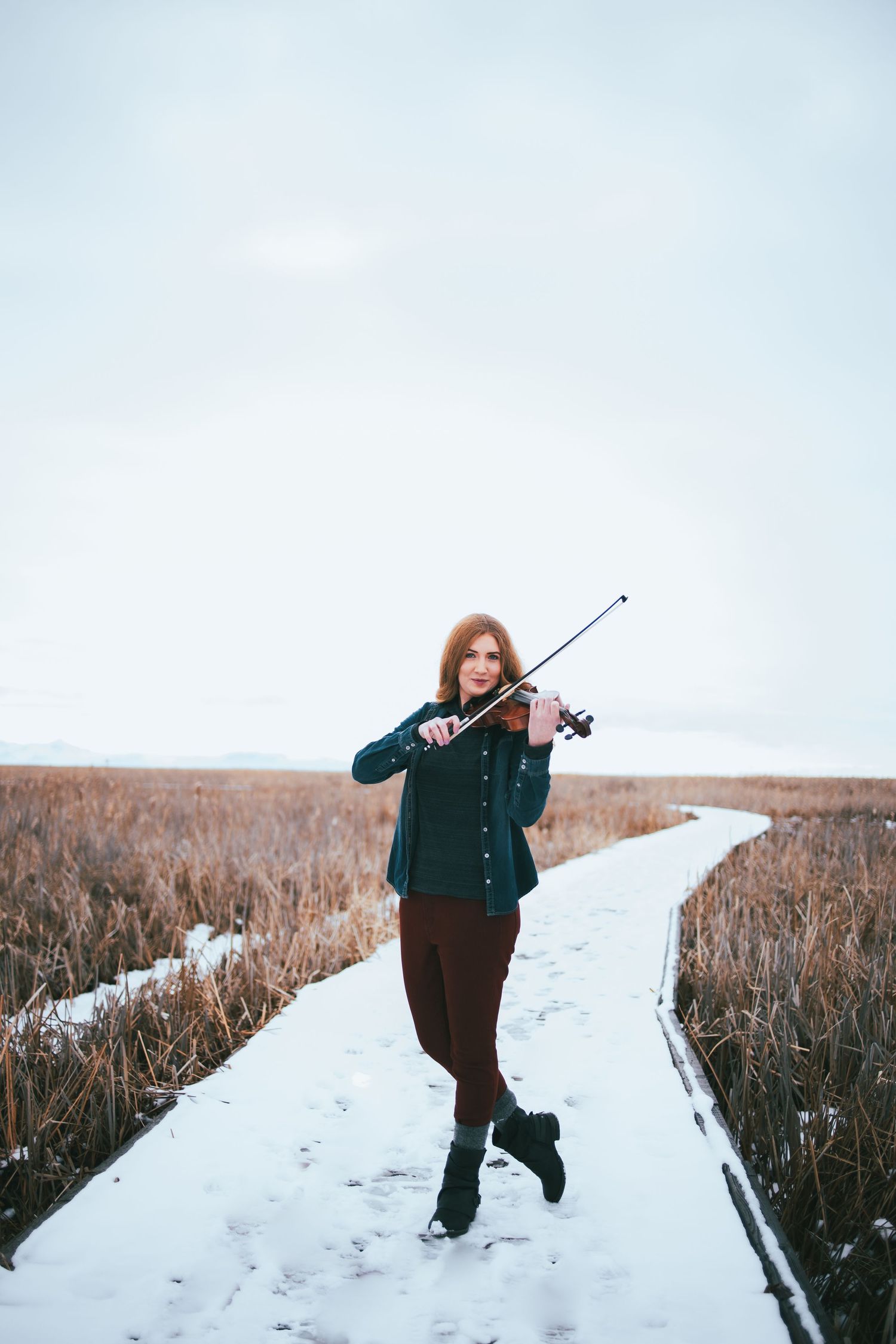 Figure walking on snow-covered boardwalk through winter marsh landscape.