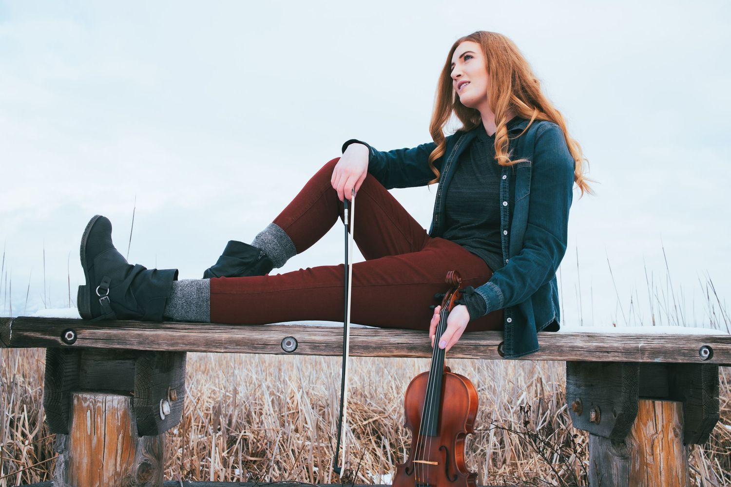 Person relaxing on wooden dock with violin in winter attire.