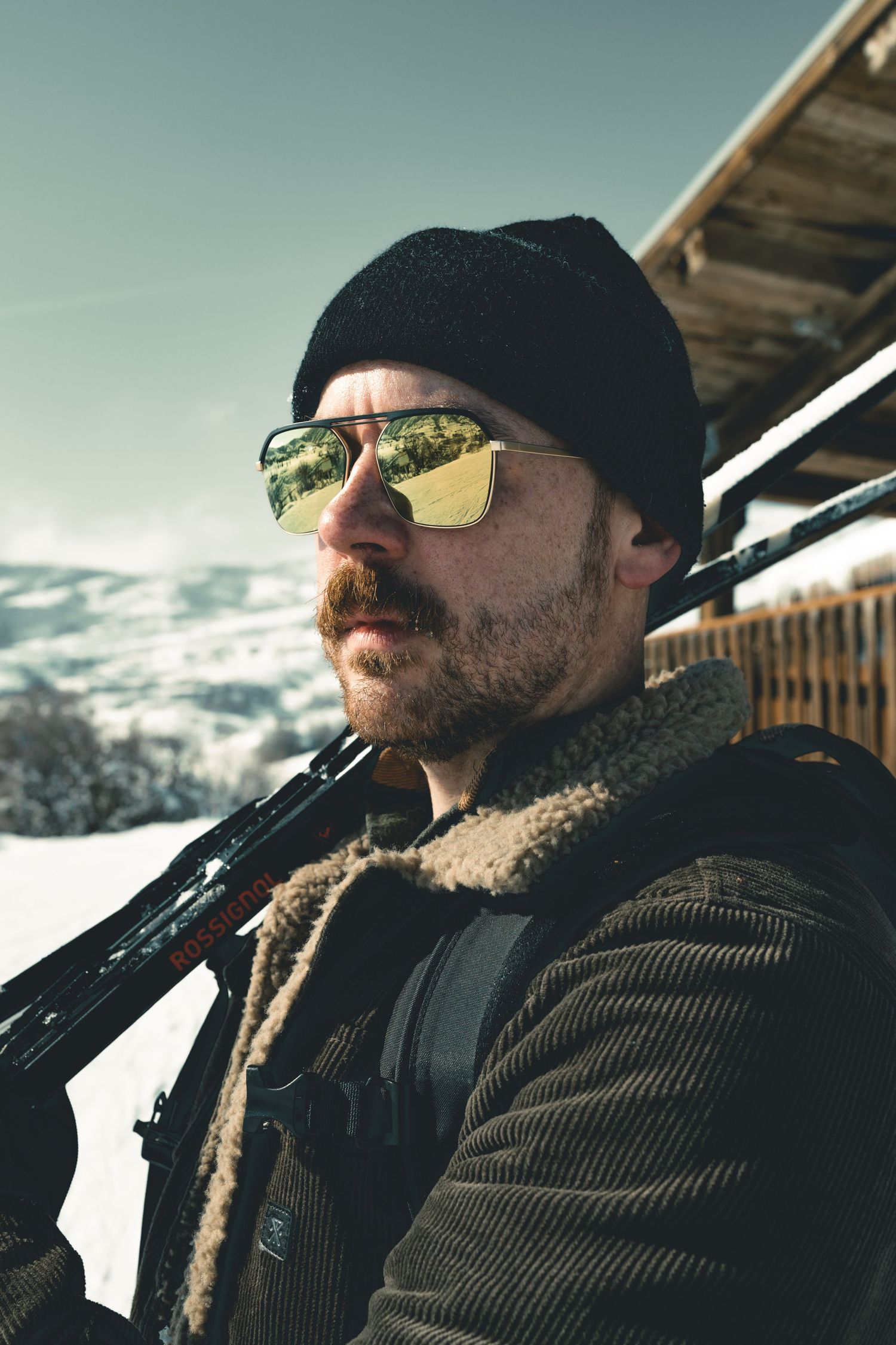 Winter portrait of someone in a black cap and coat against snowy mountain backdrop.