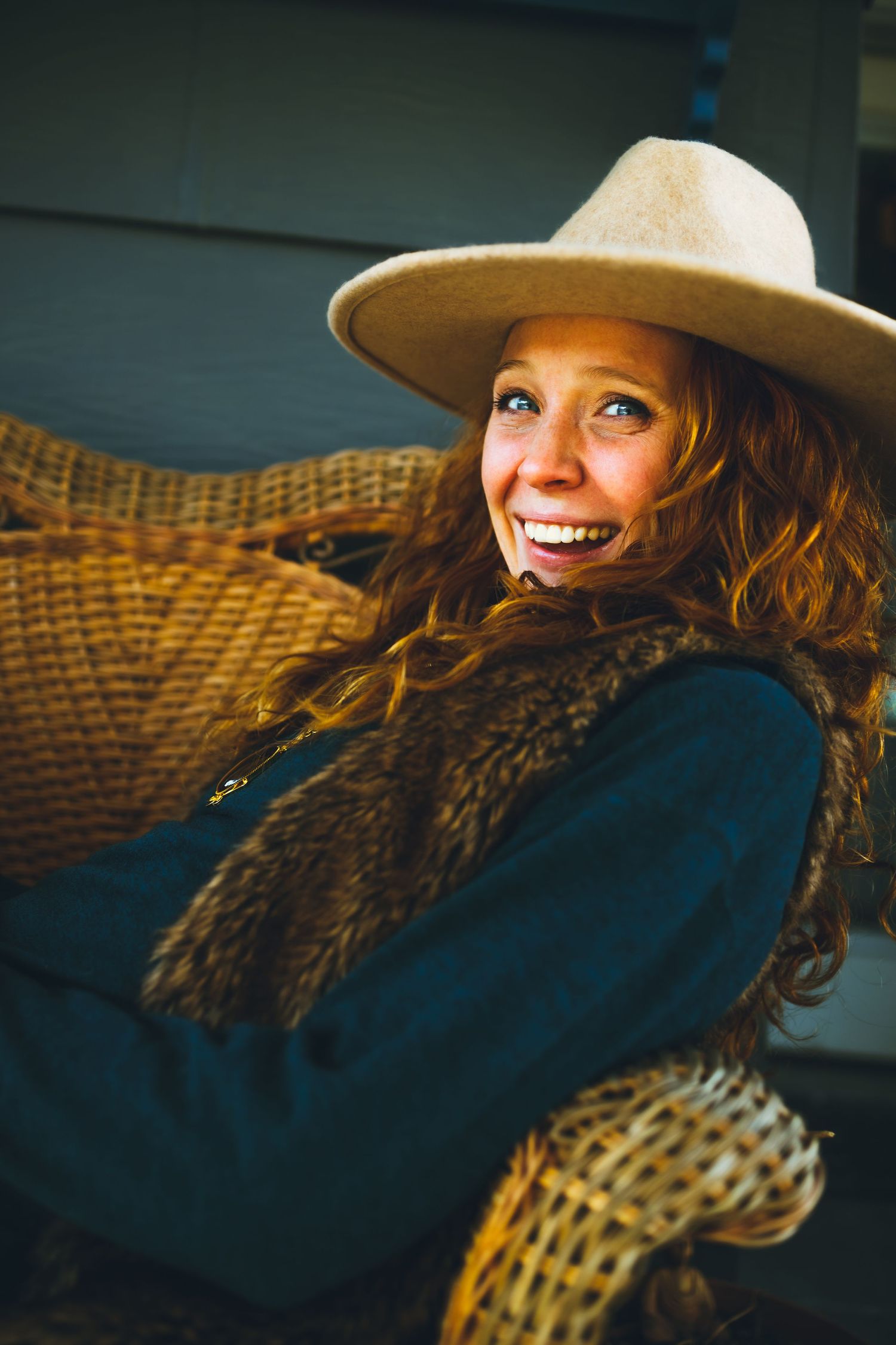 Candid portrait on wicker furniture showing relaxed pose in tan hat and dark clothing.