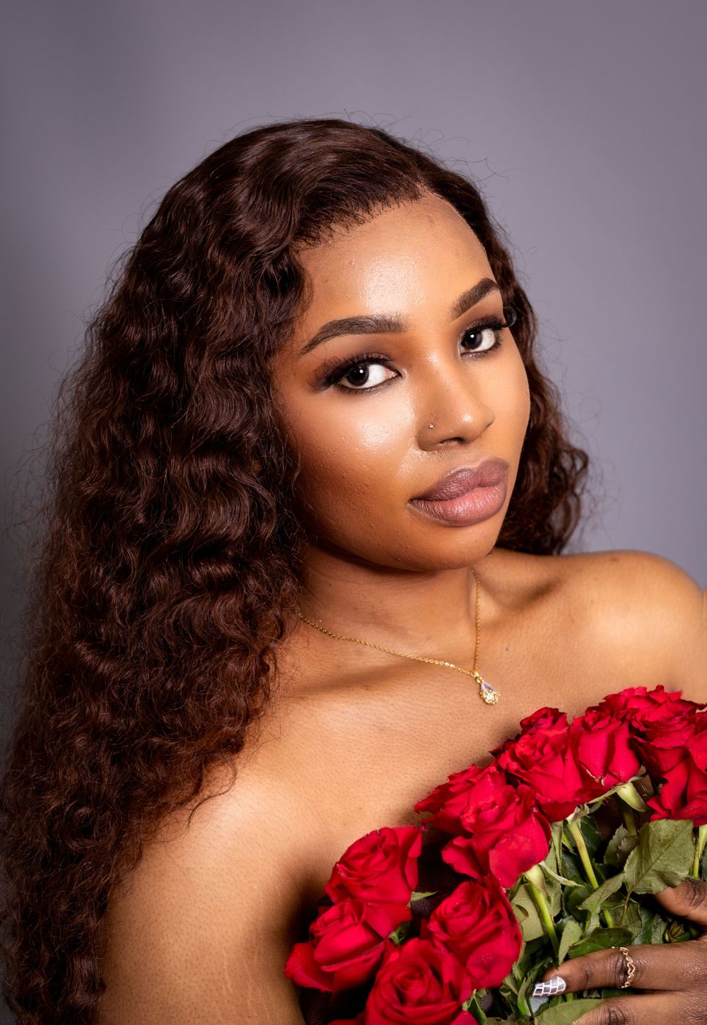 Glamorous beauty portrait with red roses and curled hair against purple background .