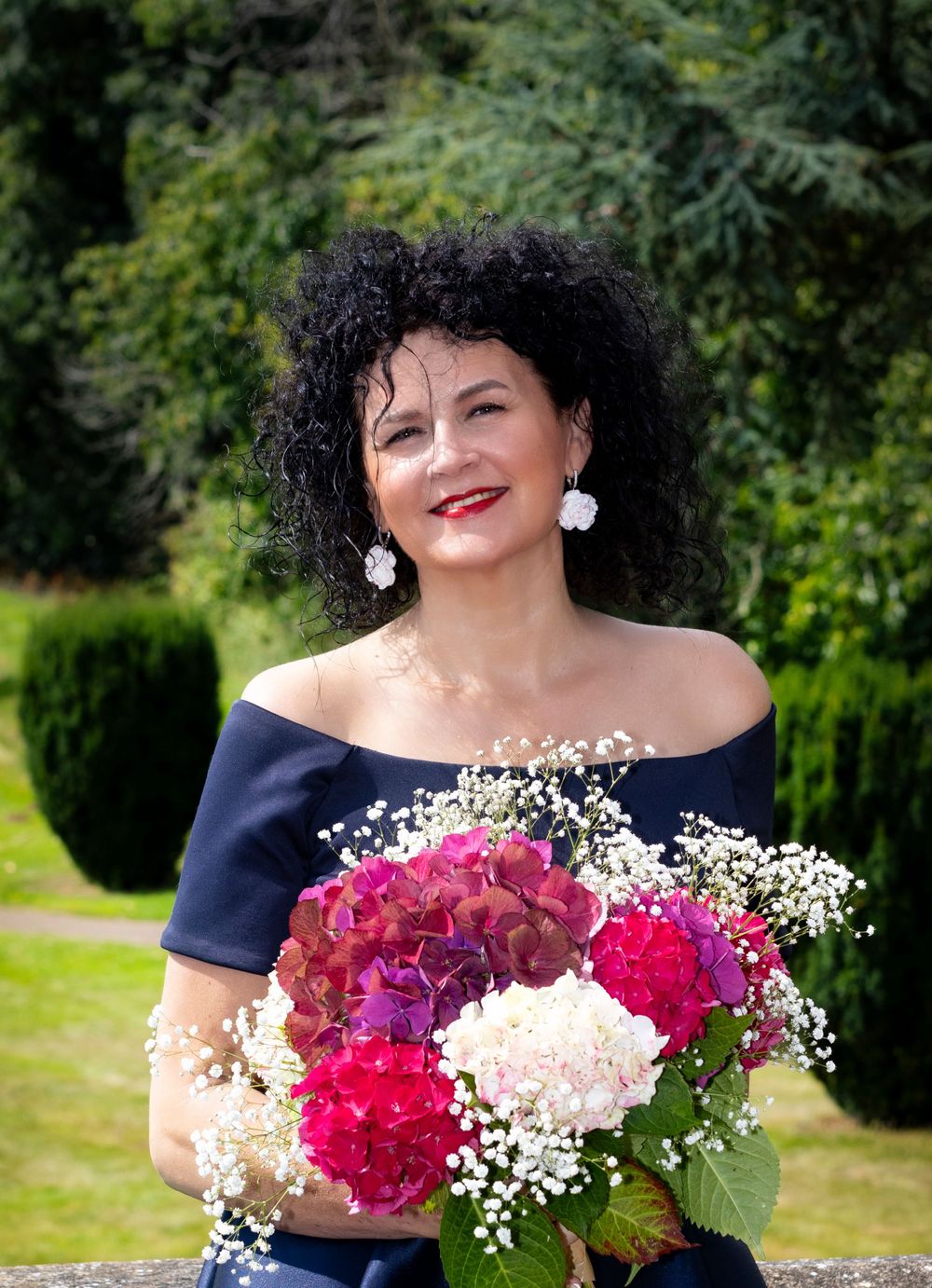 A person in an off-shoulder navy dress holds a colorful bouquet with pink flowers and baby's breath.