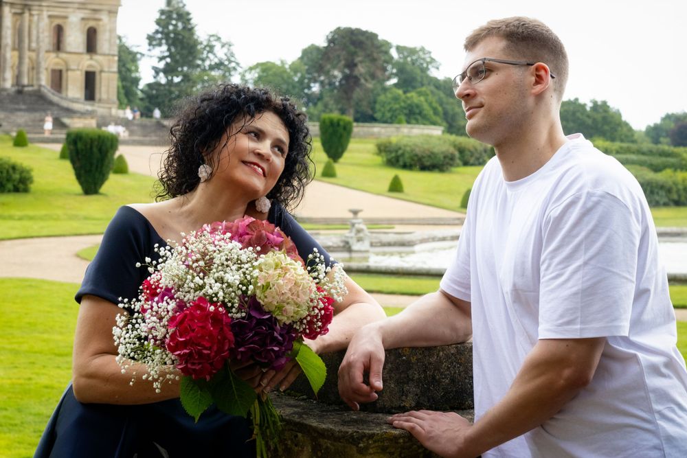 Couple enjoying a moment together in front of a grand estate with floral bouquet.
