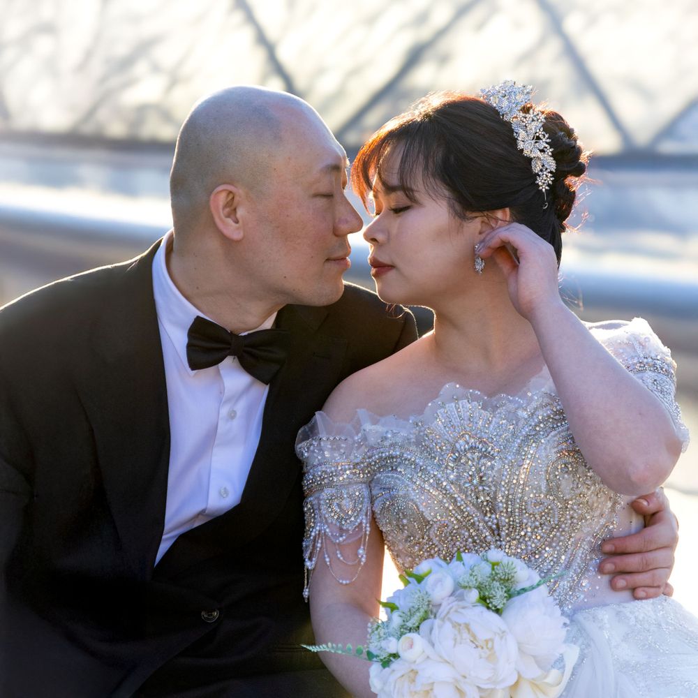 A romantic wedding couple shares an intimate moment outdoors, with the bride wearing a beaded dress and holding a bouquet.