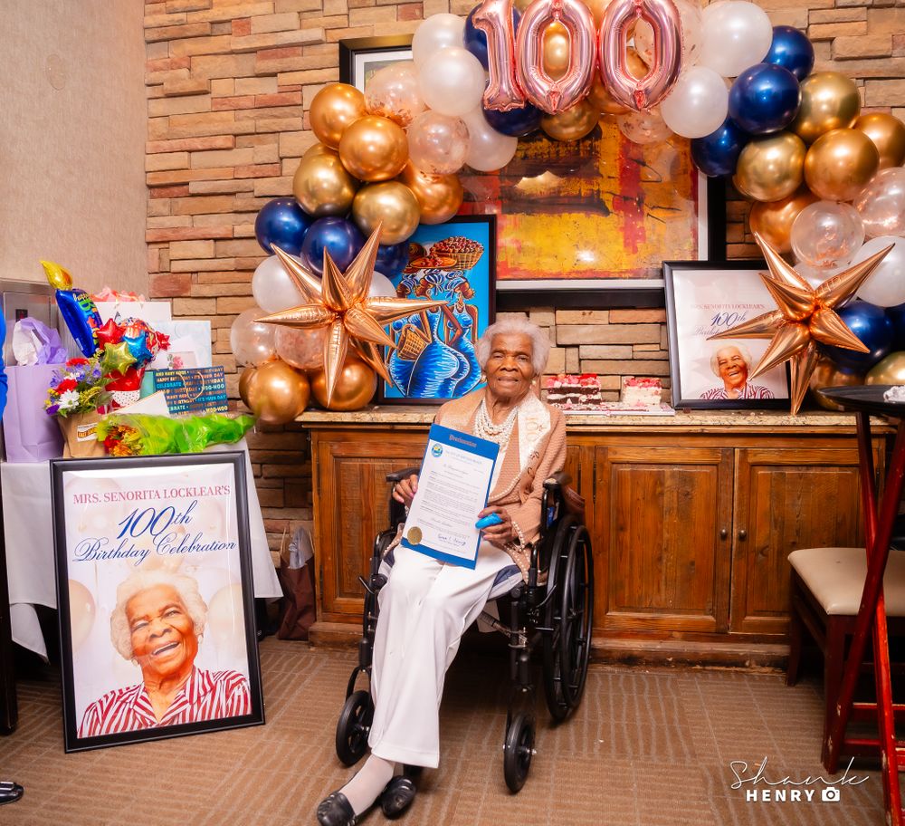 100th birthday celebration with gold and blue balloons decorating a brick-walled room.