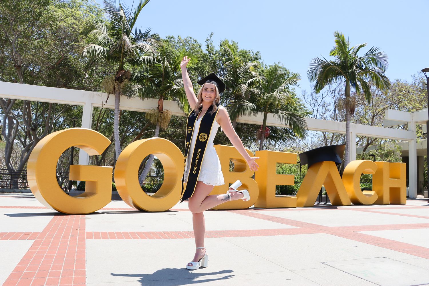 Graduate takes creative photos with large yellow CSULB letters on campus.