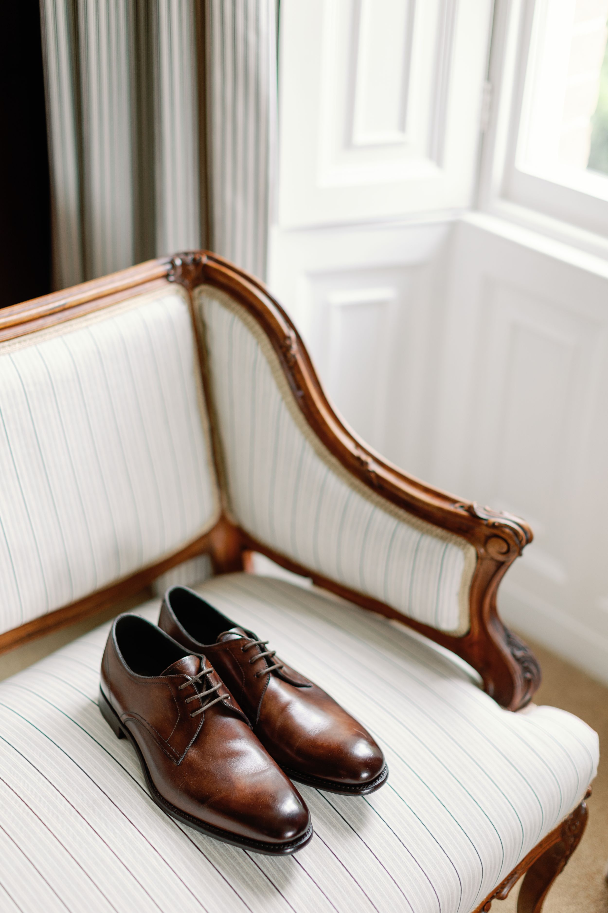 Brown leather dress shoes placed on an antique white upholstered chair.