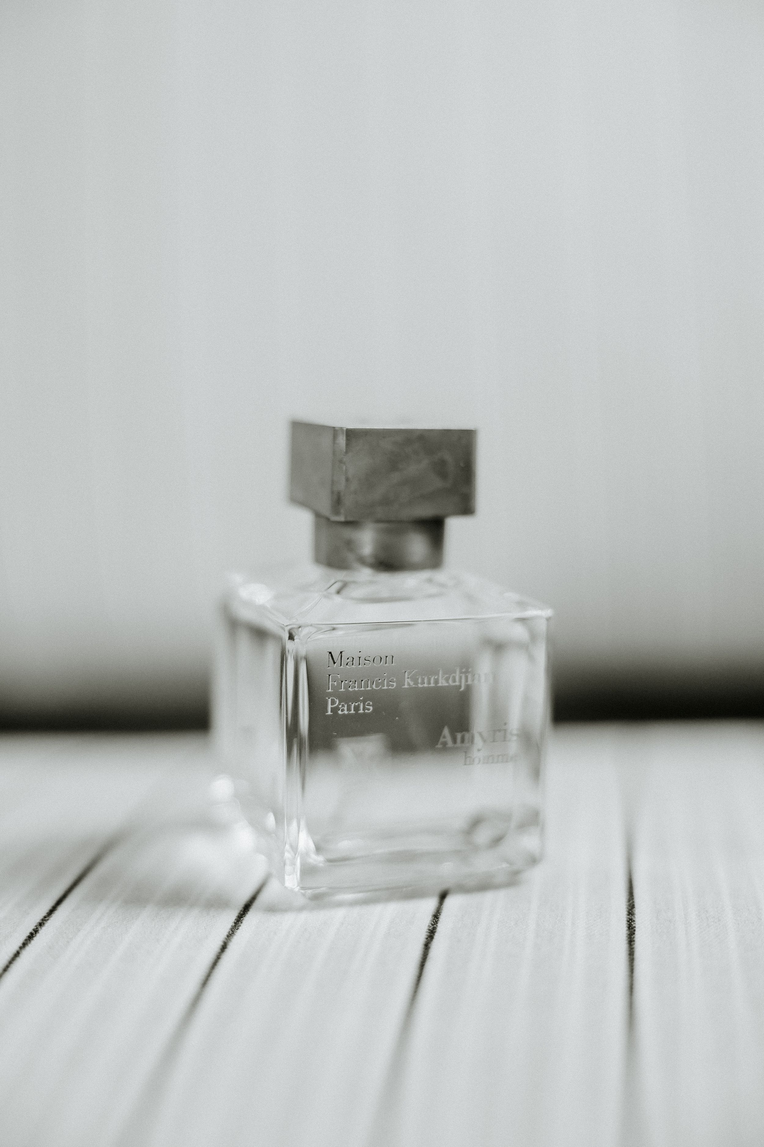 Minimalist glass perfume bottle on white wooden surface in black and white.