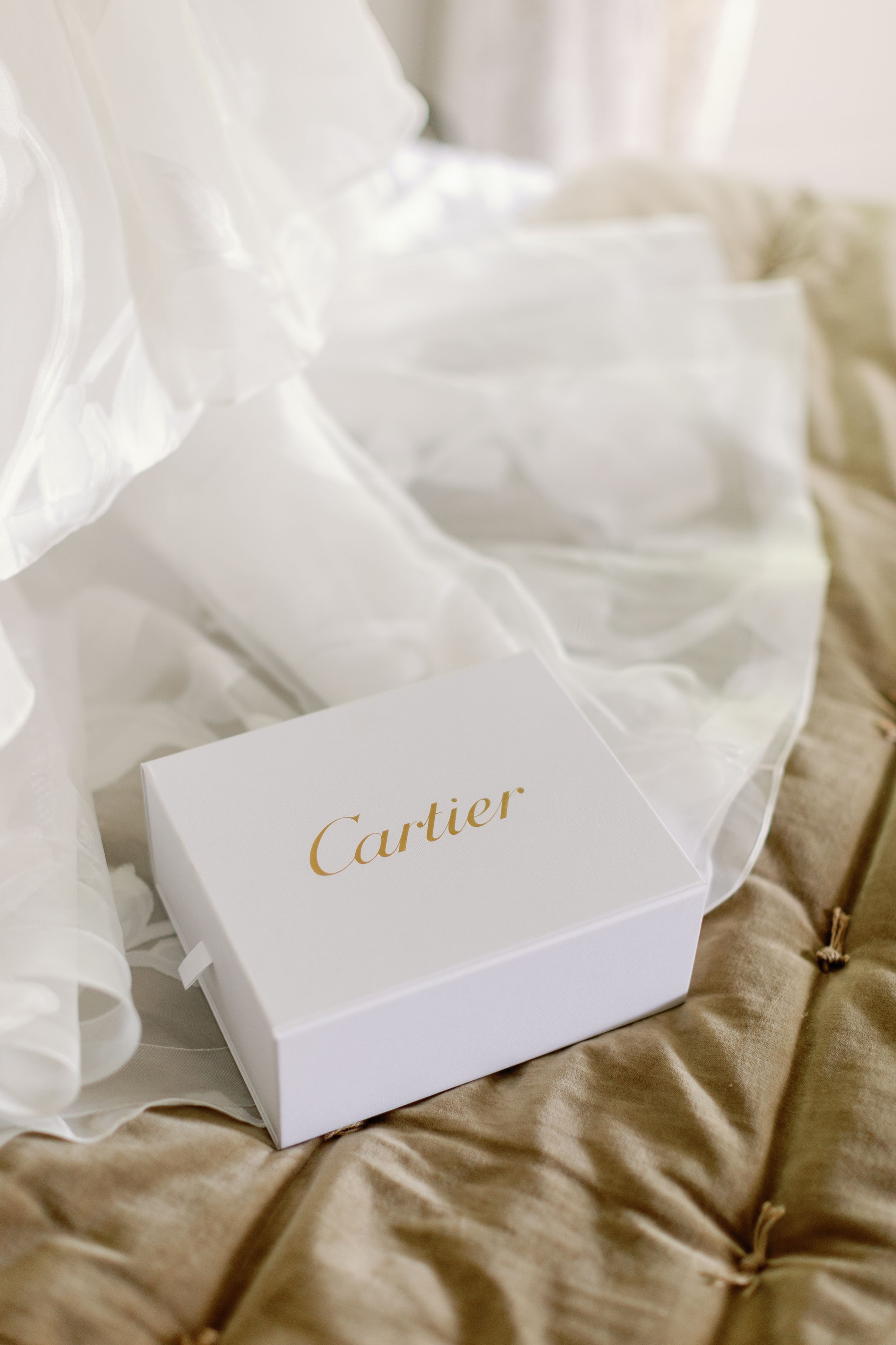 White Cartier gift box with gold lettering resting on soft silk fabric.
