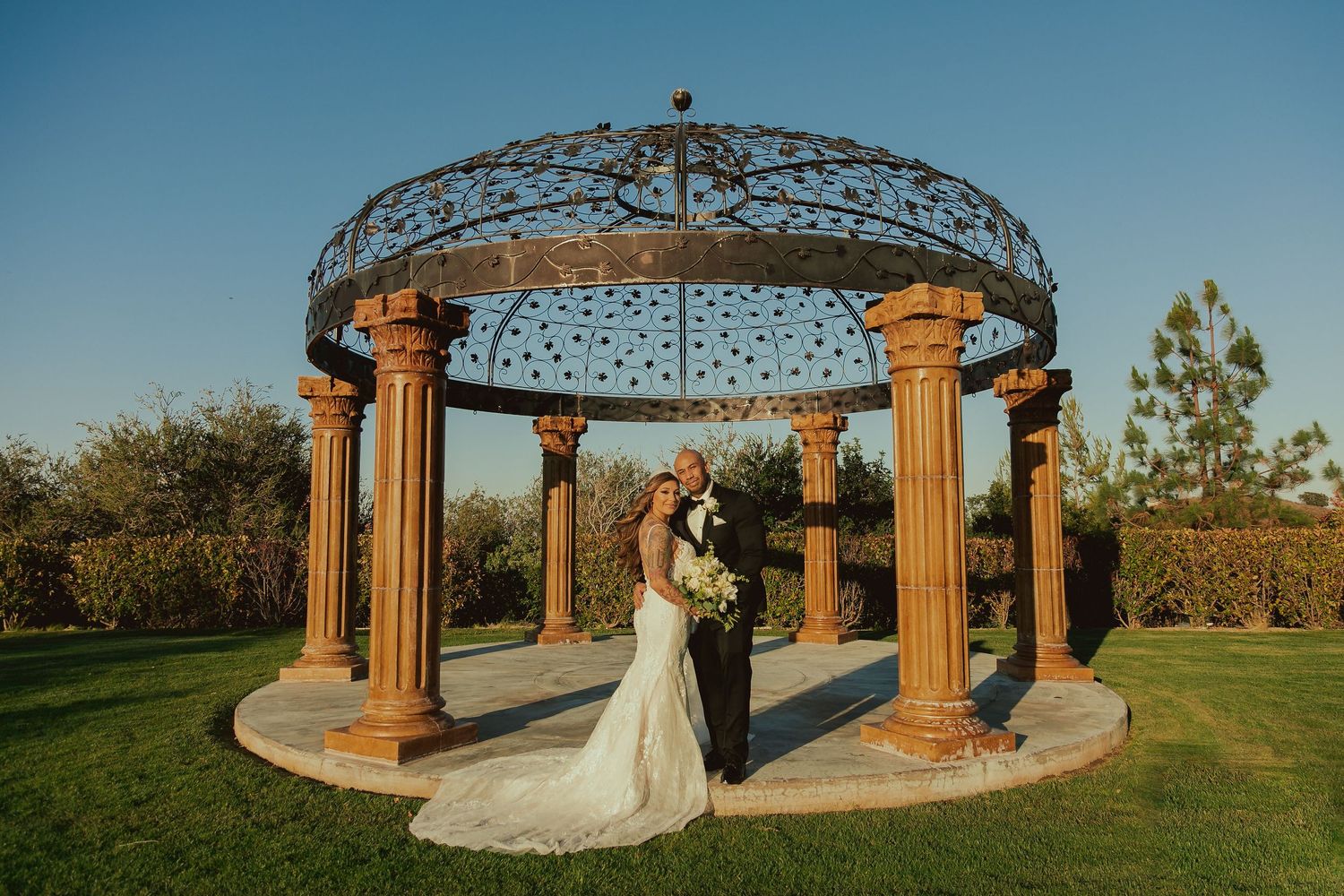A couple sharing a romantic moment under an ornate gazebo in a garden setting.