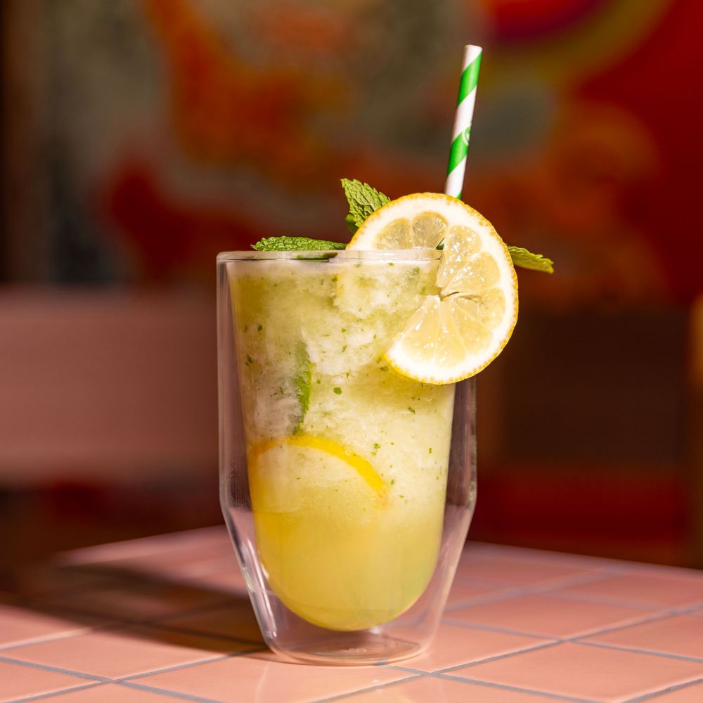 mango smoothie sitting on pink tiles with a dappled green and red background