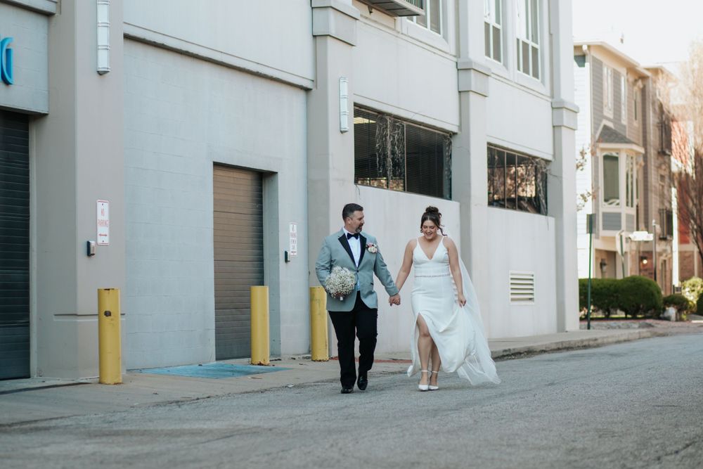 A couple in wedding attire walks hand in hand down an urban street with industrial buildings in the background in Indianapolis Indiana.