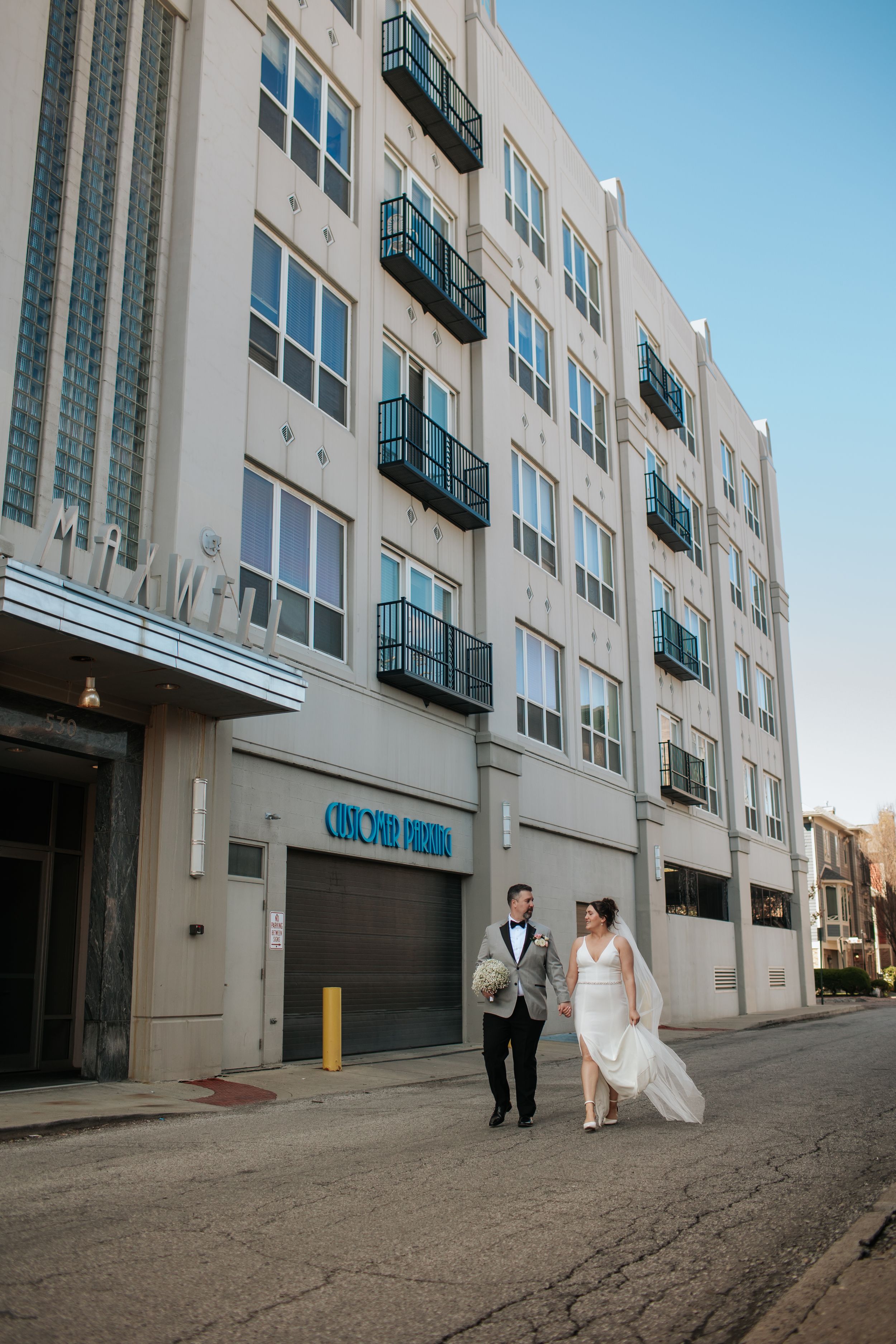 A wedding couple walks along a gray urban alley with tall apartment buildings on one side in Indianapolis Indiana.
