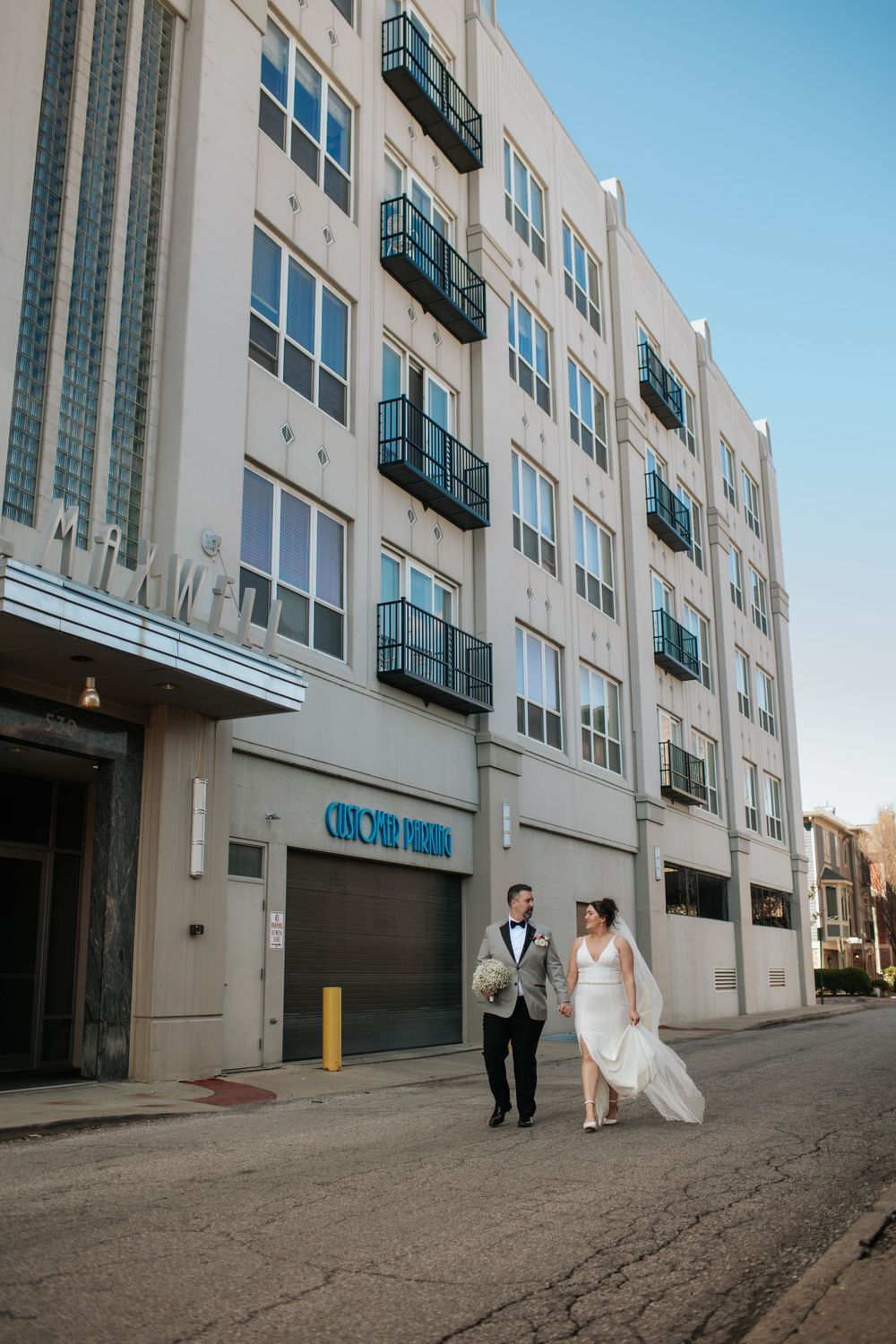 A wedding couple walks along a gray urban alley with tall apartment buildings on one side in Indianapolis Indiana.