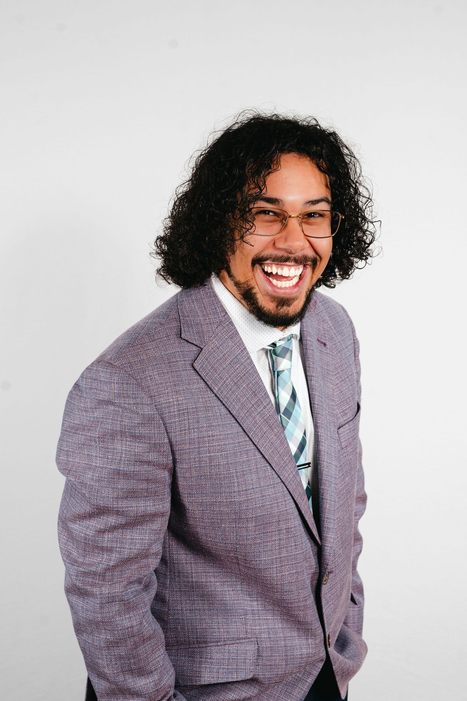 Professional portrait of someone in a gray suit and patterned tie laughing joyfully against a white background.