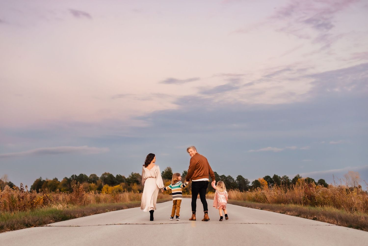 A family walks together on a concrete path during sunset with pink and purple sky overhead.