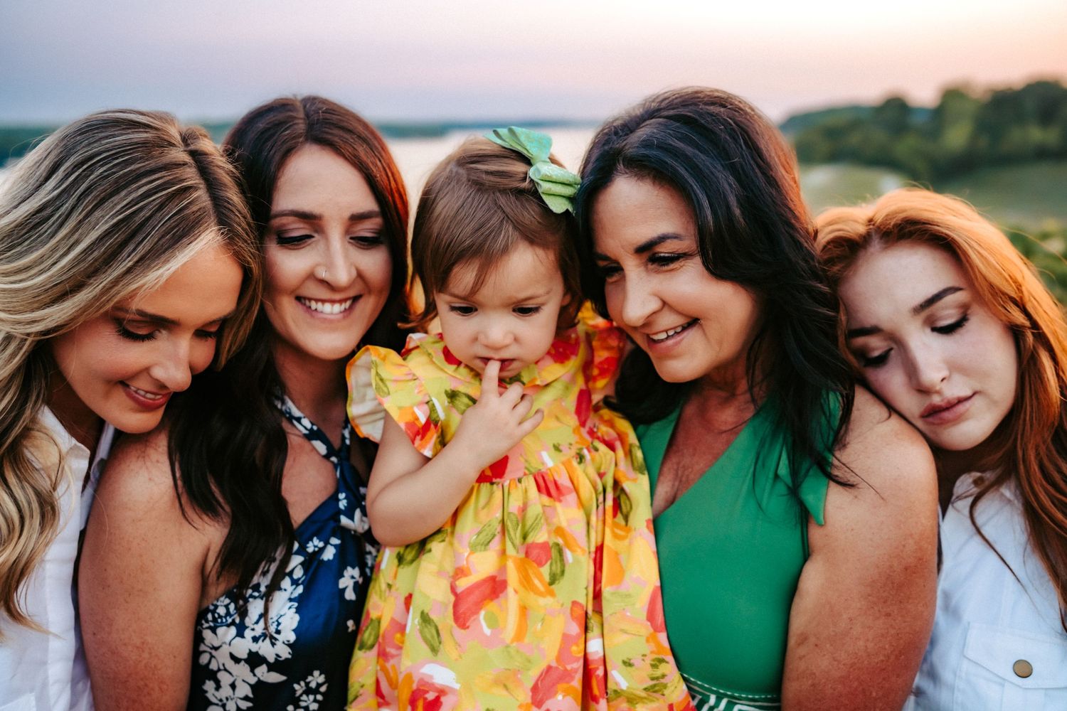 A group of women and a small child in a yellow dress gather close together at sunset for a warm outdoor photo.