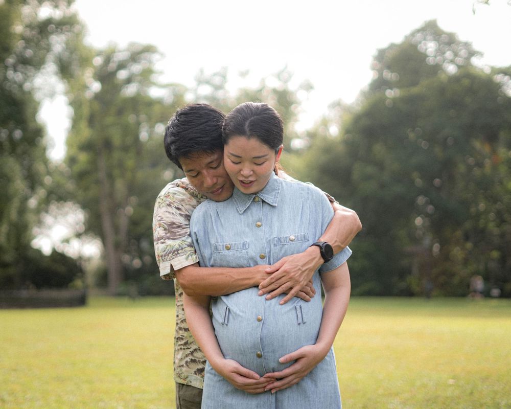 A tender embrace during a maternity photoshoot in a sunlit park.