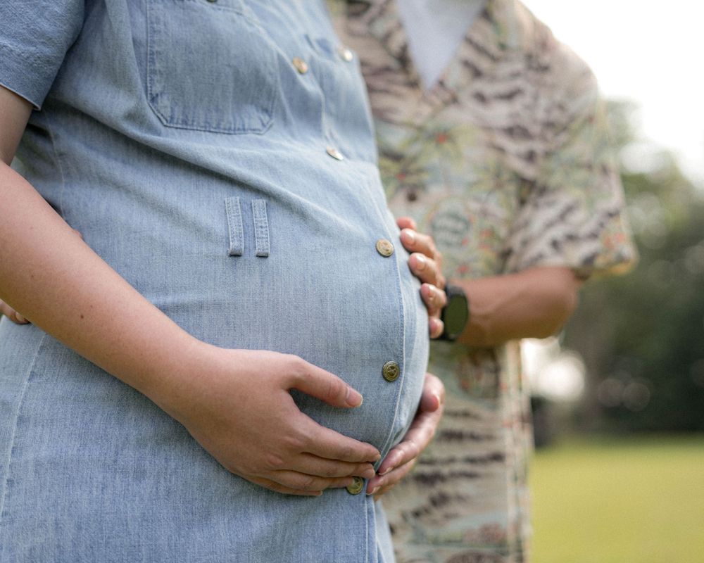 Close-up shot of hands cradling a pregnant belly in a denim dress.