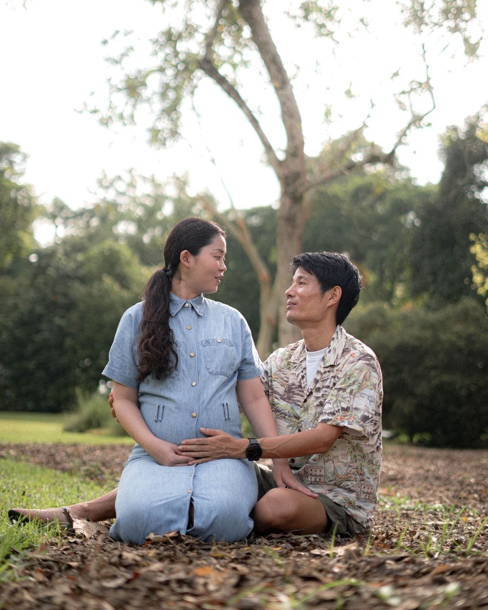 A couple sits on fallen leaves during an outdoor maternity photoshoot.