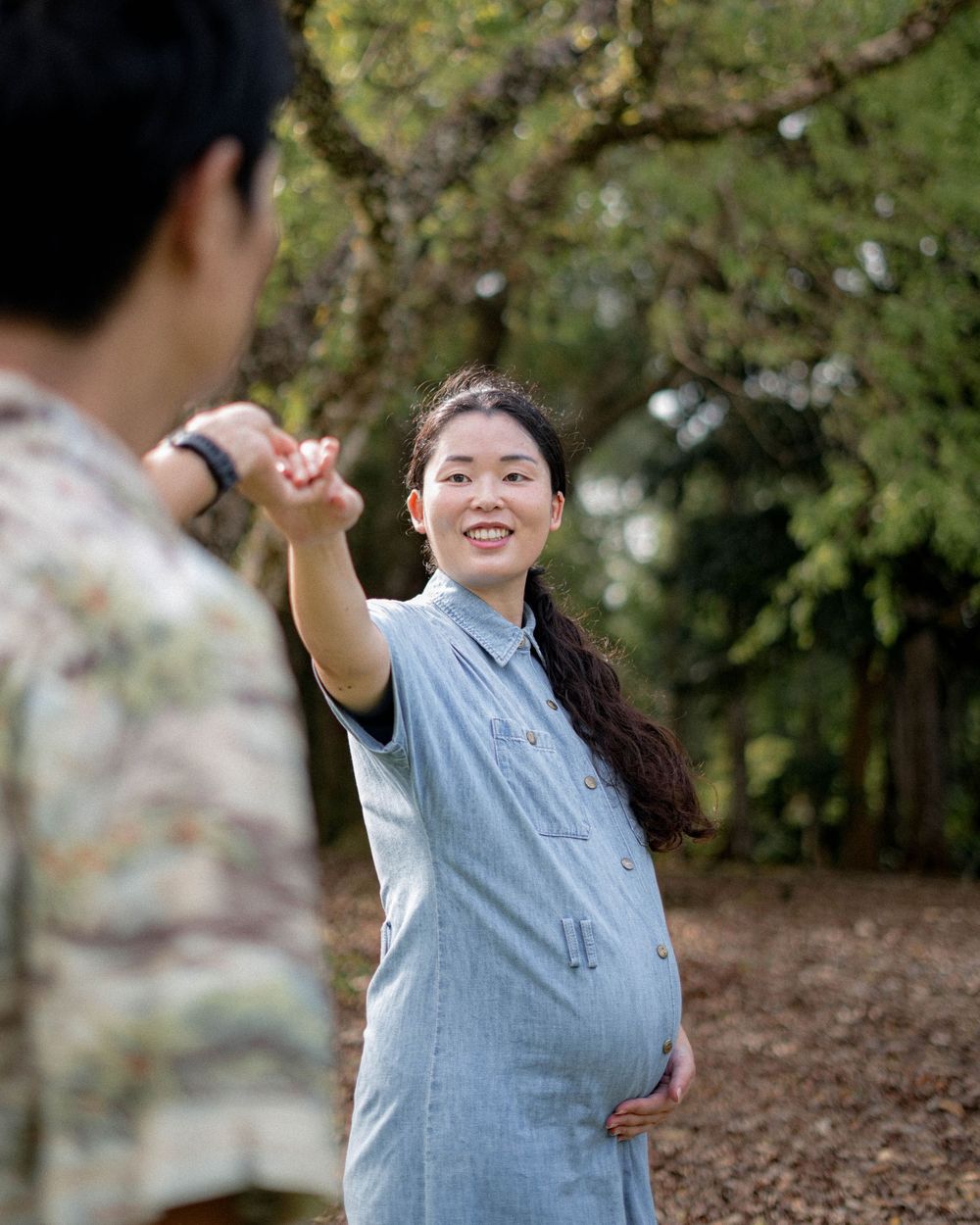 A person in a blue dress stretches out their hand while standing in a garden setting.